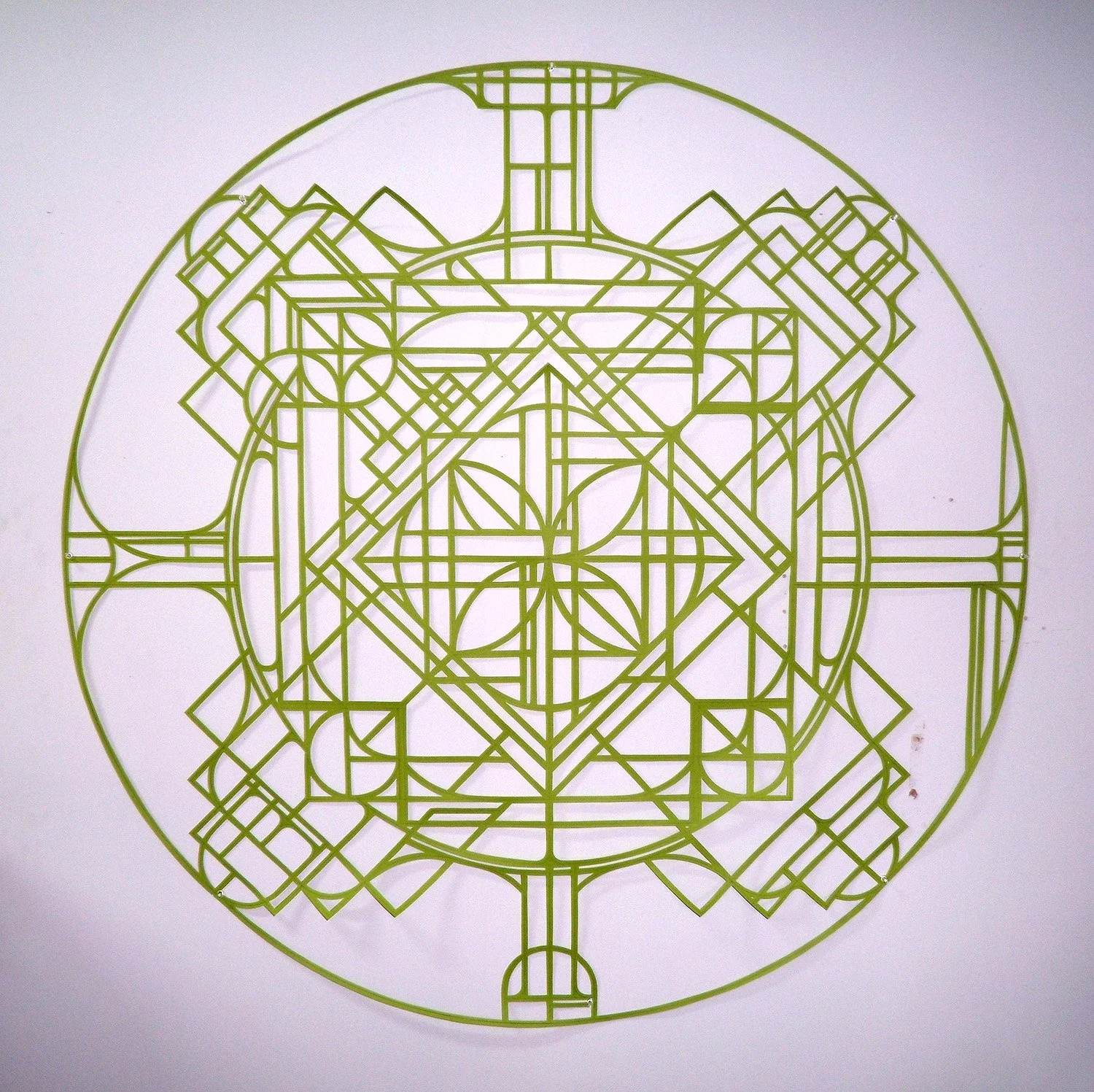 abstract geometric mandala artwork from cut green paper on a white wall