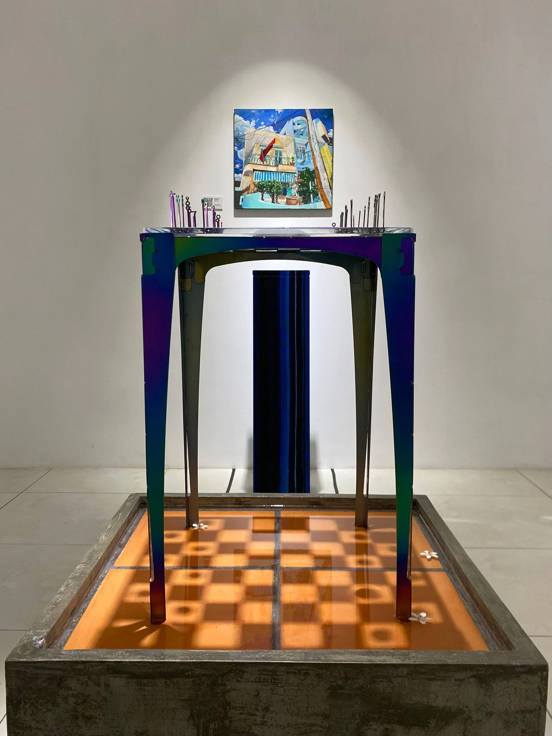 sculptural chess table filled with water on base in gallery with painting of house behind