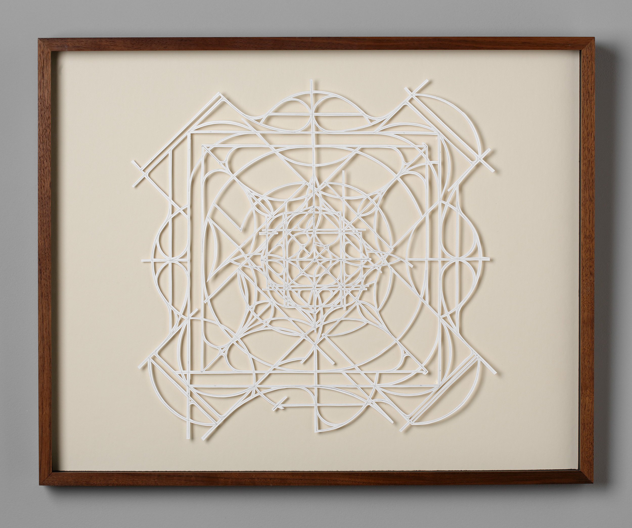 abstract geometric mandala artwork from finely cut white paper on a sand colored surface with wood frame