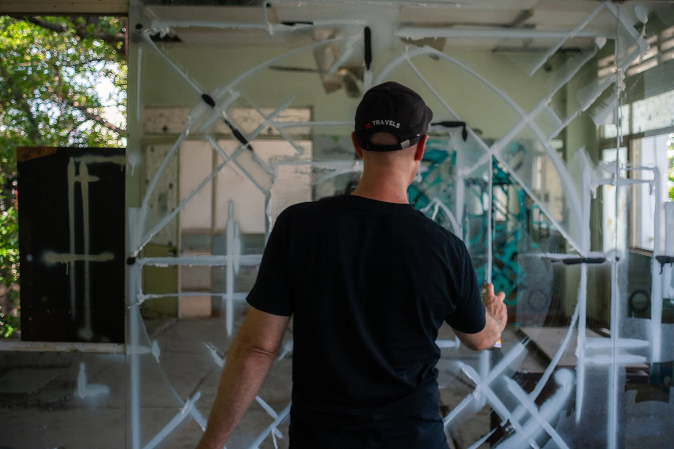 man painting an abstract geometric mandala on a mirror with spray paint in the room of an abandoned building