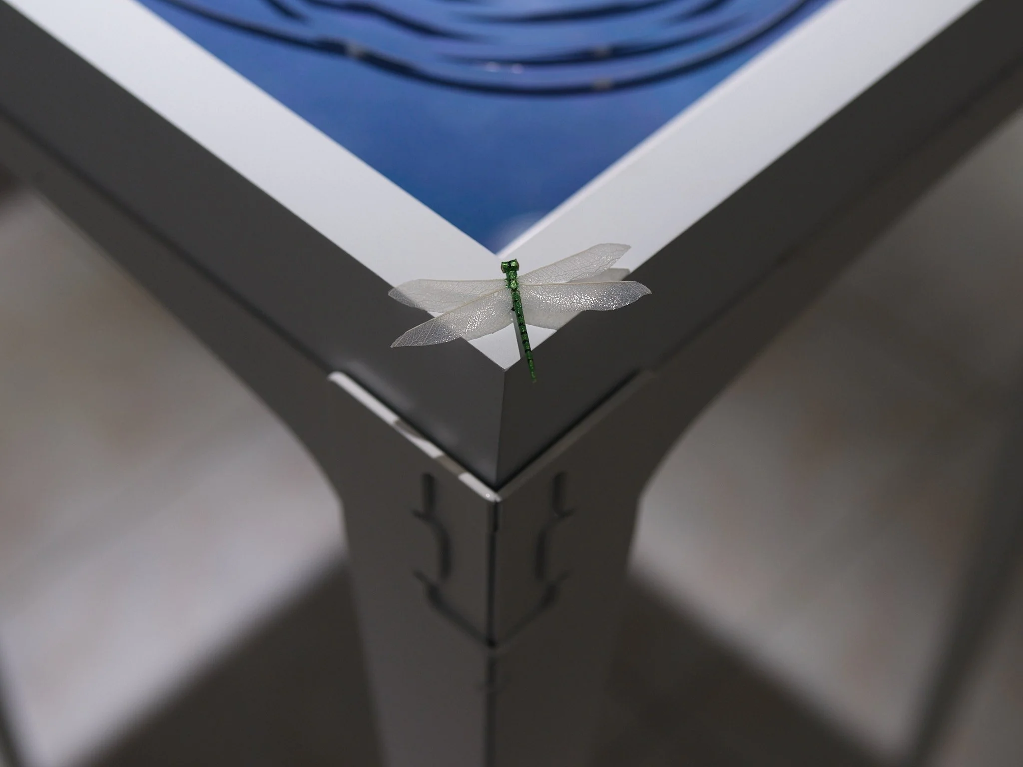 miniature sculpture of a dragonfly on the corner of a white and blue table