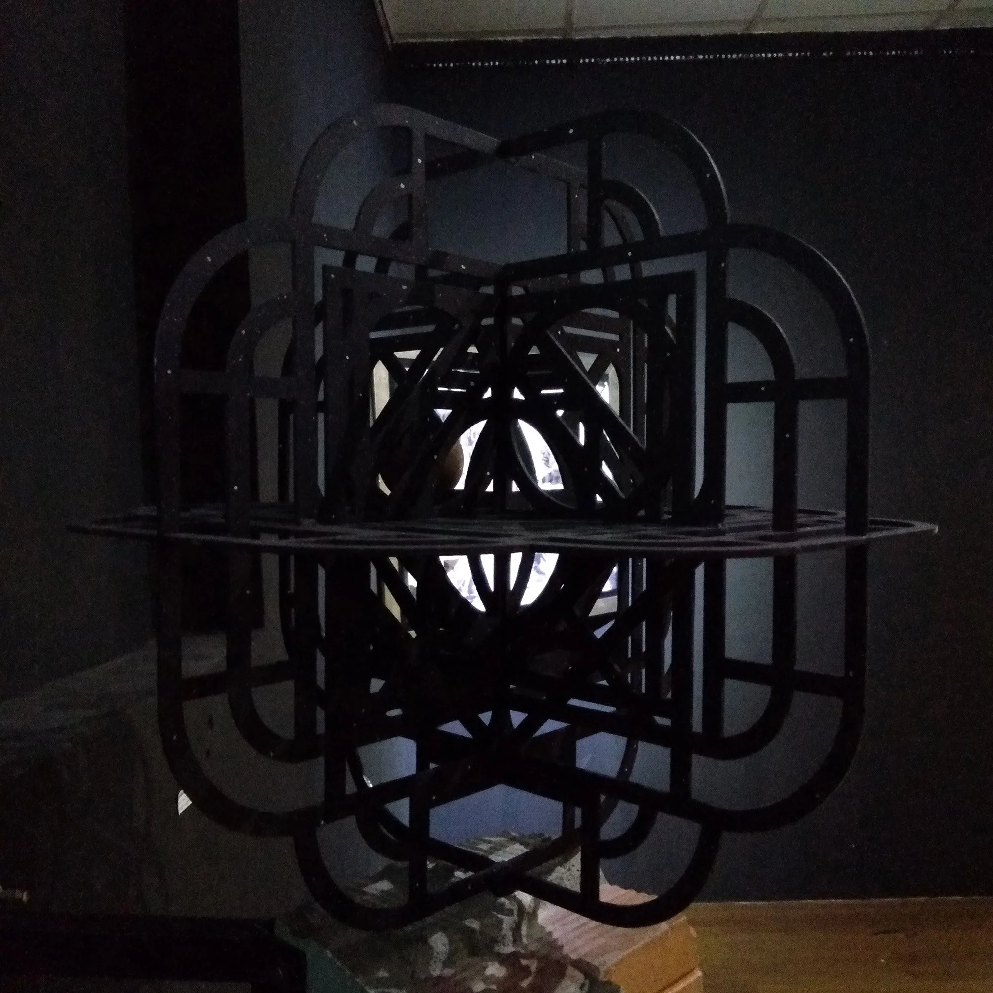 abstract geometric metal sculpture painted black in a black gallery