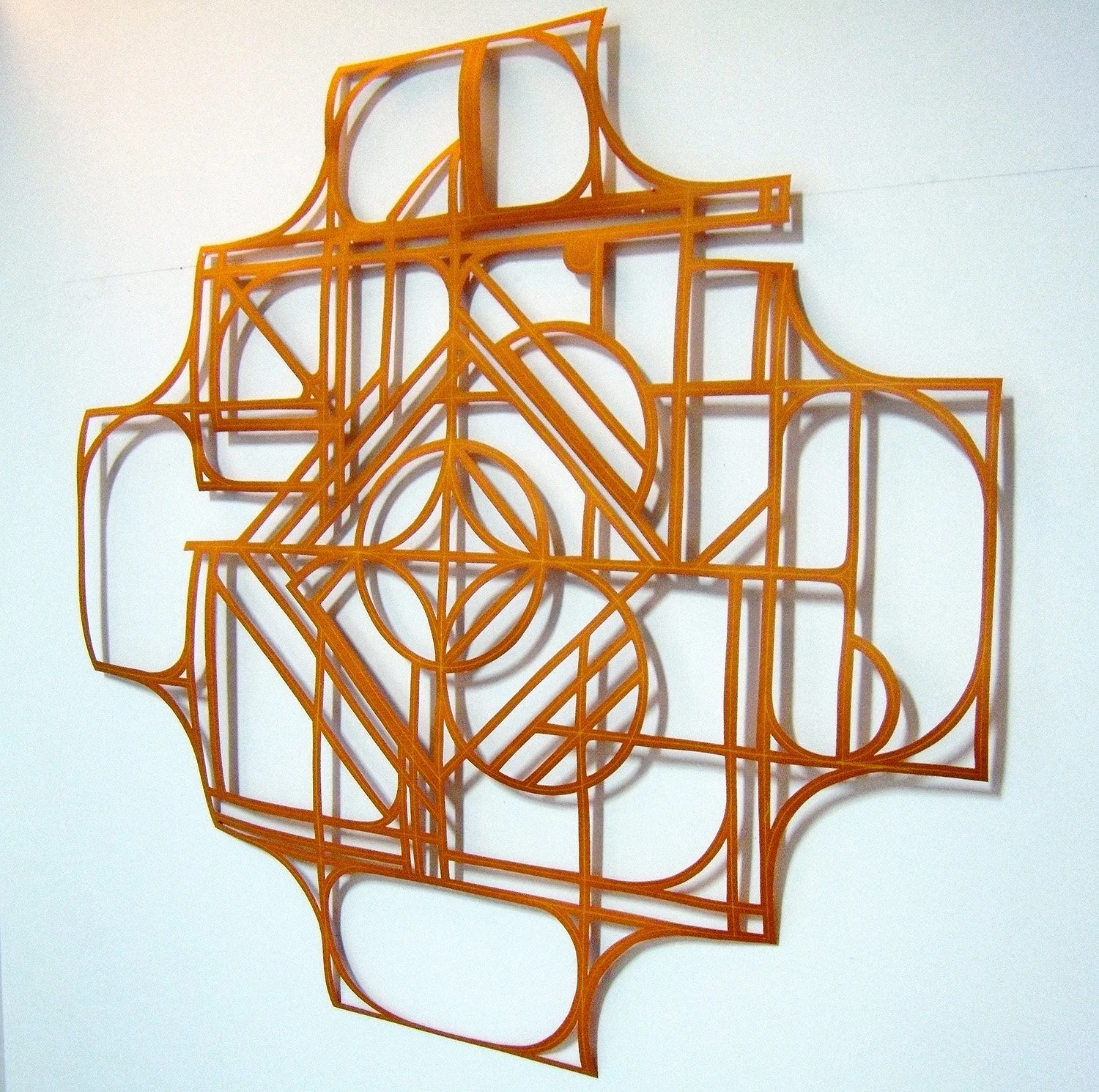 abstract geometric mandala artwork from cut orange paper on a white wall