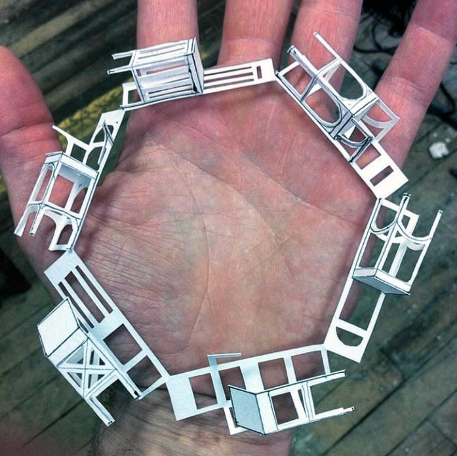 a ring of miniature paper chairs resting in an open hand