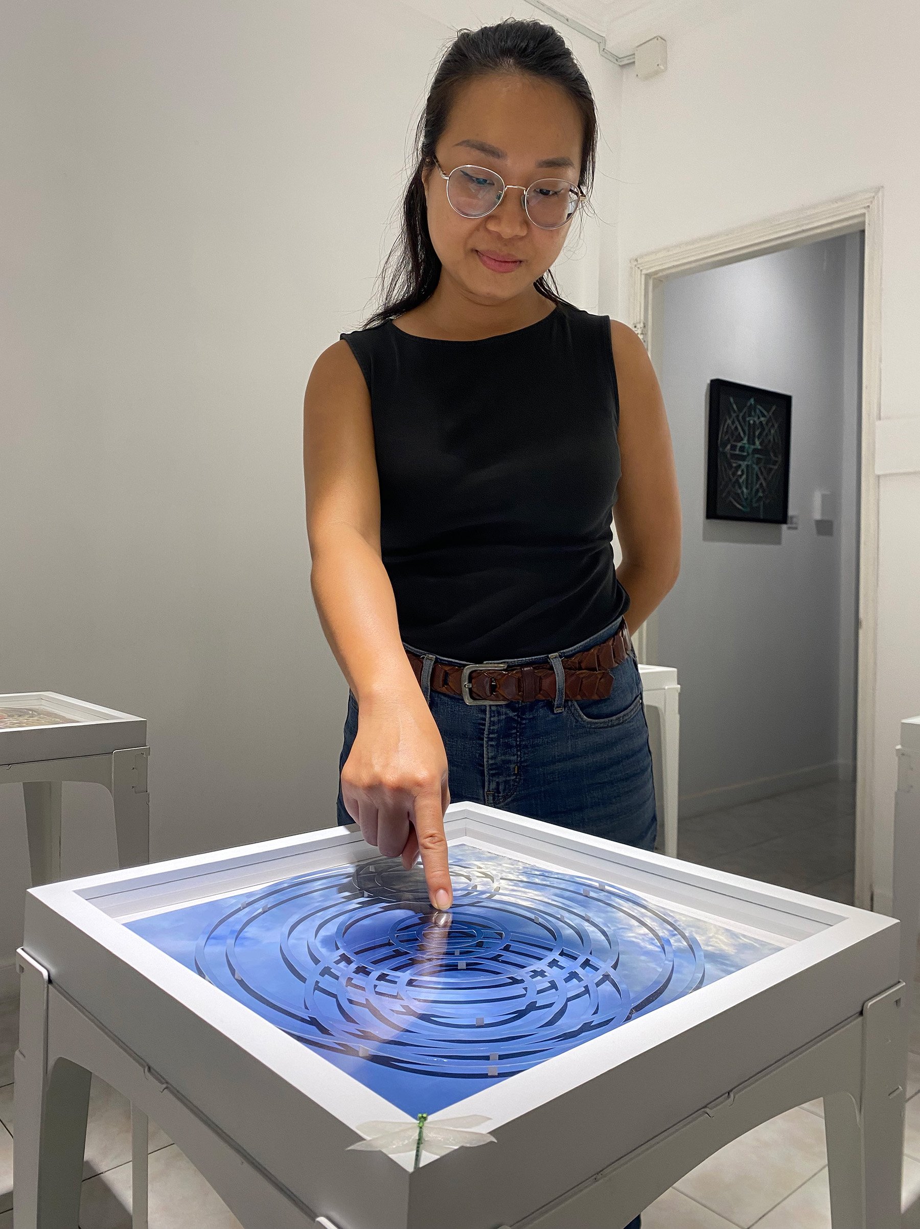 woman pointing at photo collage on table of the sky where photo looks agitated by rain drops on water
