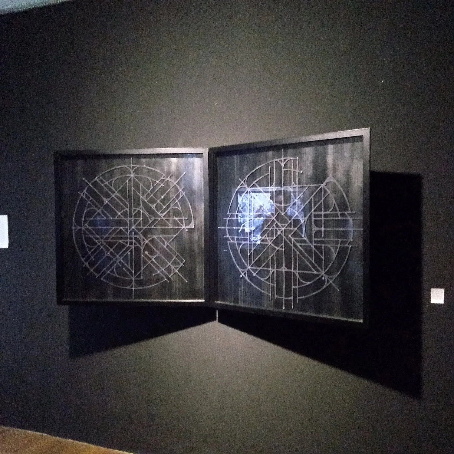 an abstract geometric paper cut diptych with black frames on a black gallery wall