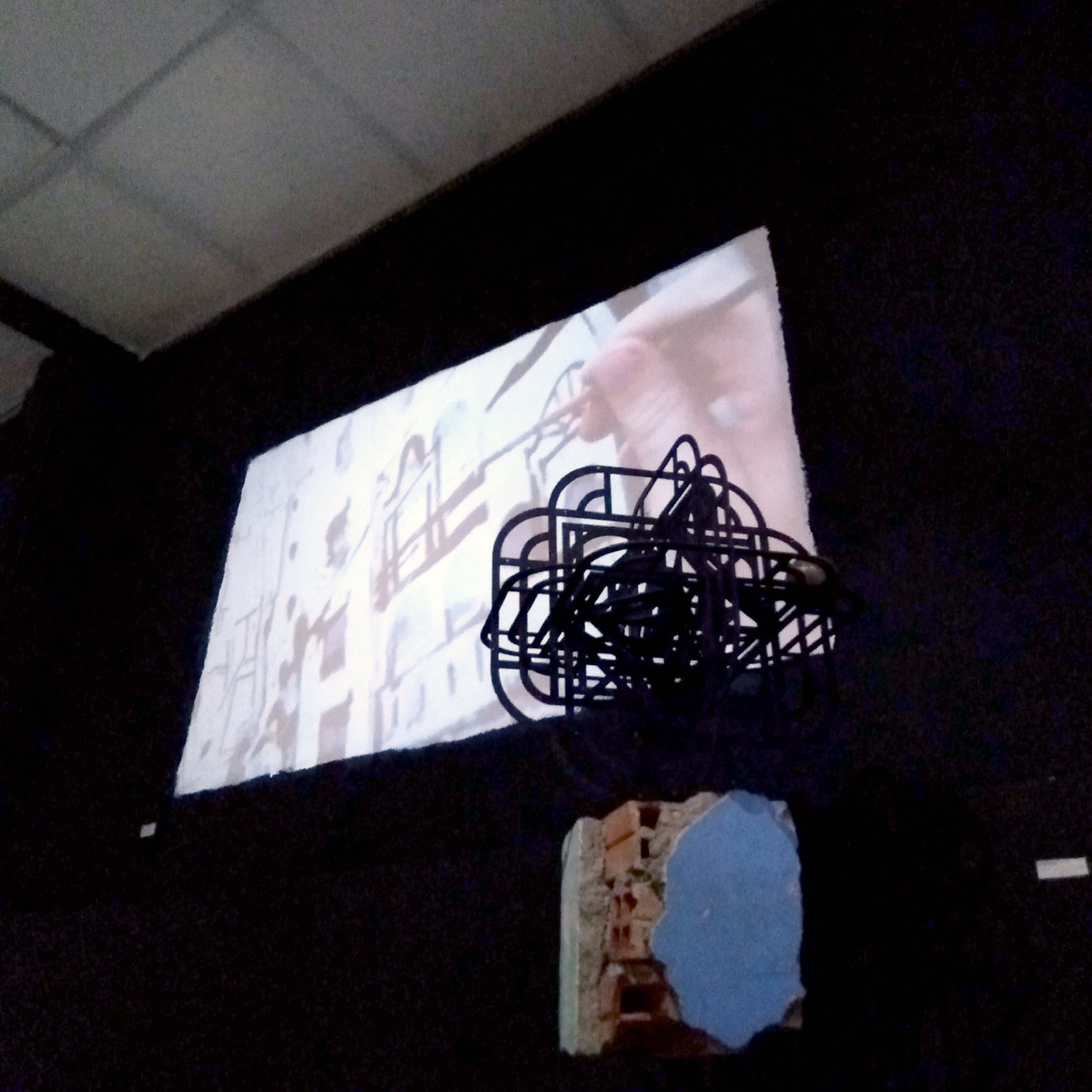 gallery installation in black room with video projection above a geometric sculpture