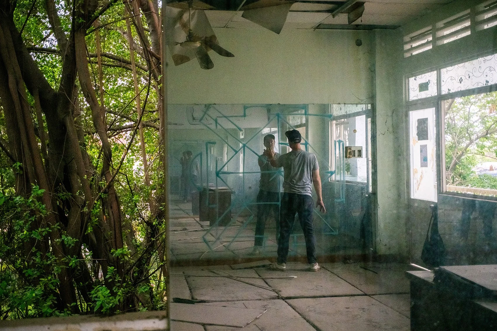 man painting on a mirror with spray paint in the room of an abandoned building