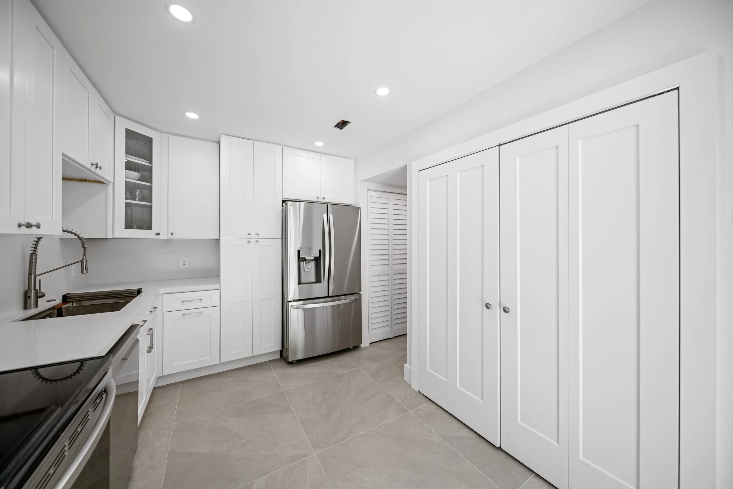 A modern white kitchen with white cabinets, a stainless steel refrigerator, and a tiled floor.