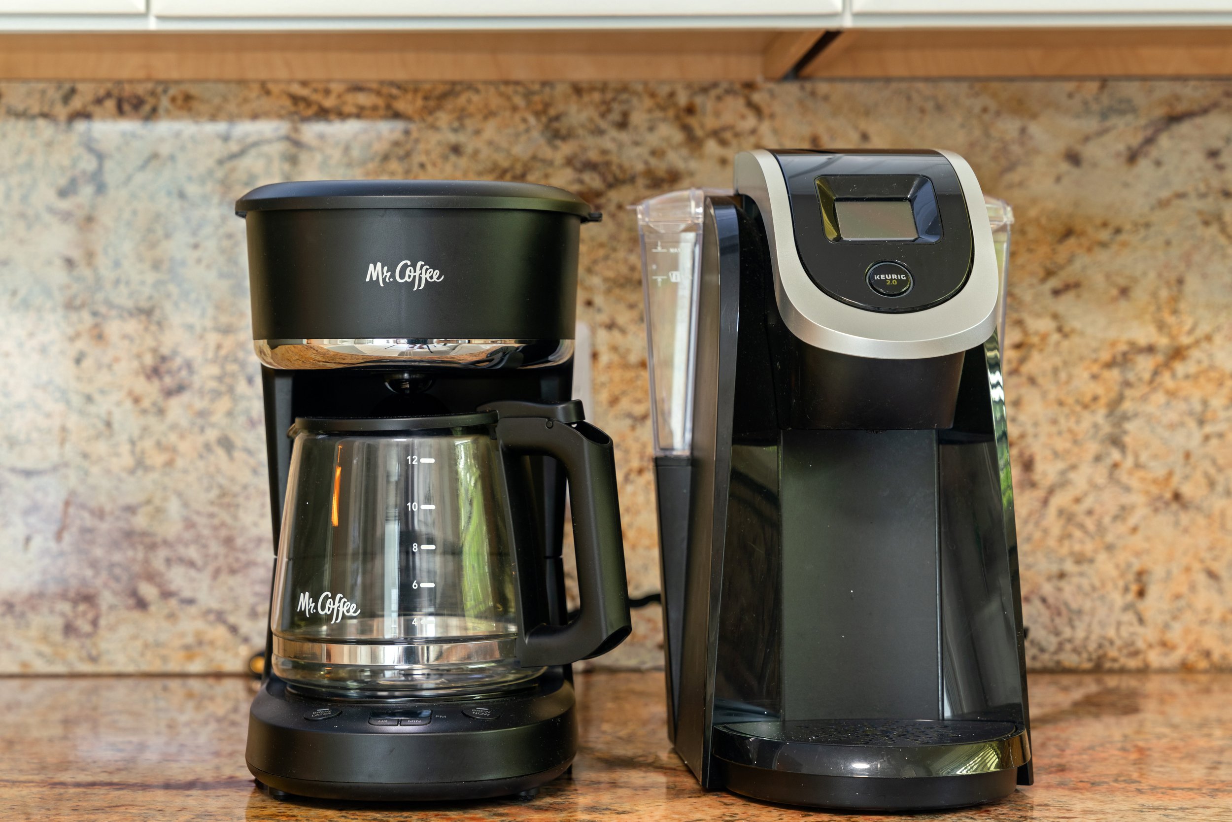 A coffee maker and a Keurig machine on a kitchen countertop with a granite backsplash.