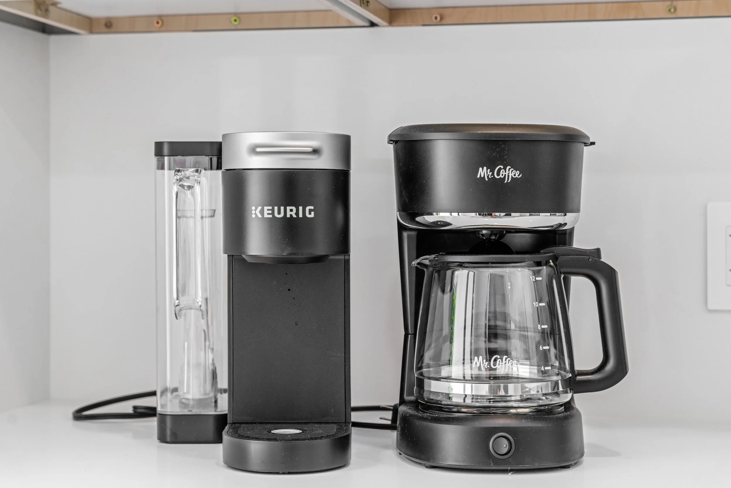 Coffee maker, electric kettle, and glass coffee pot on a white countertop in a kitchen.