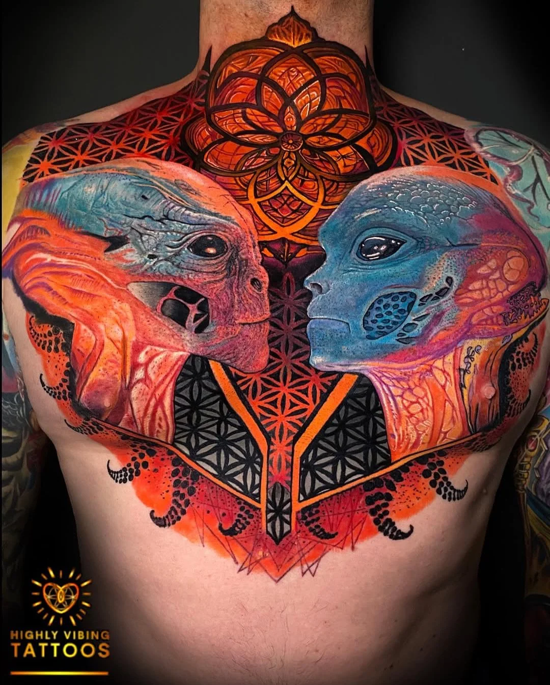 Colorful tattoo of two alien faces facing each other, surrounded by geometric patterns and a large mandala design on the neck. The tattoo features vibrant orange, blue, and black colors. Daniel Armitage, Calgary Alberta, Surrealist Tattoo Artist, YYC