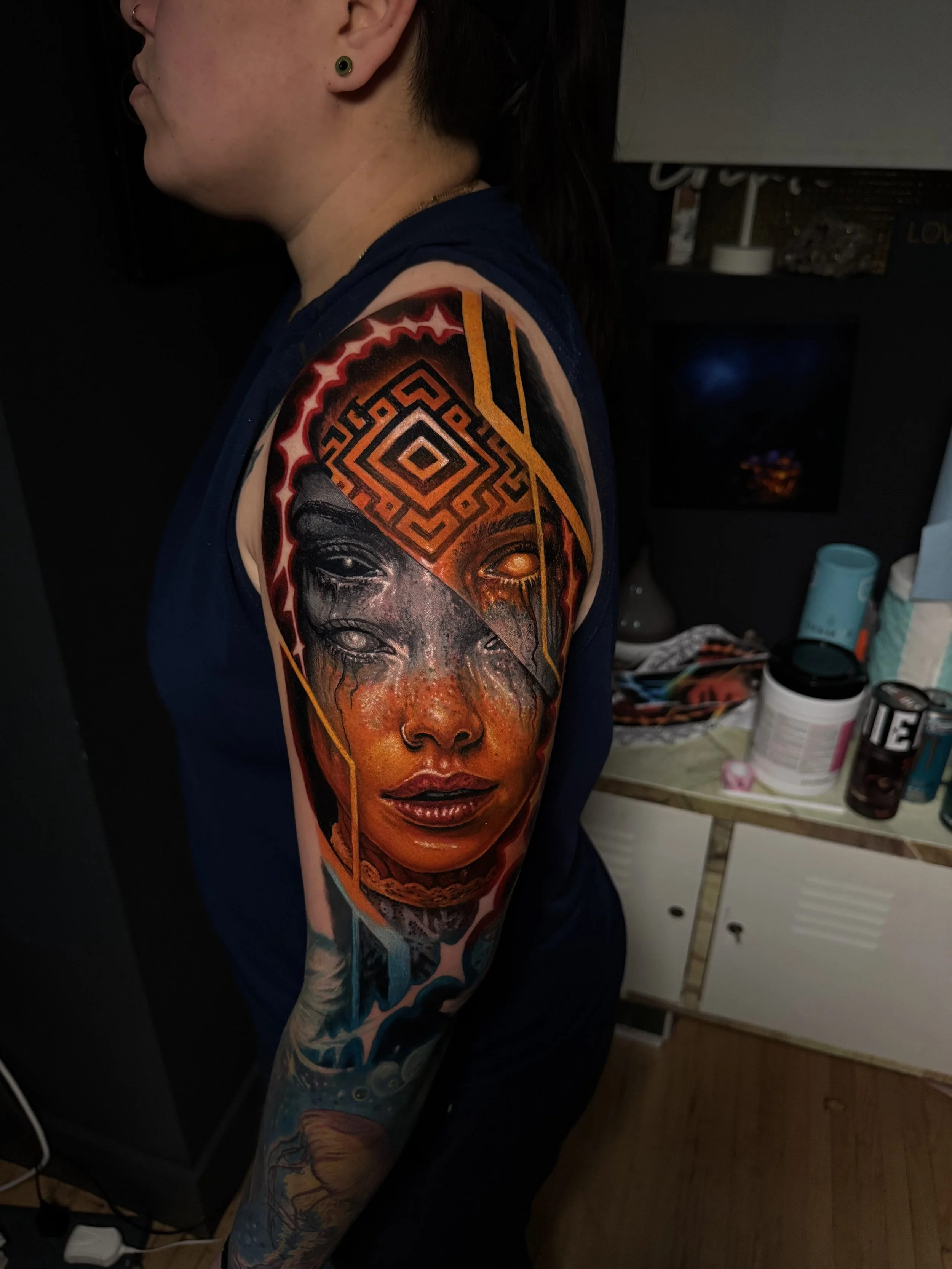 Close-up of a person's shoulder and arm with a detailed, colorful tattoo featuring faces, geometric patterns, and vibrant colors. Daniel Armitage, Calgary Alberta, Surrealist Tattoo Artist, YYC