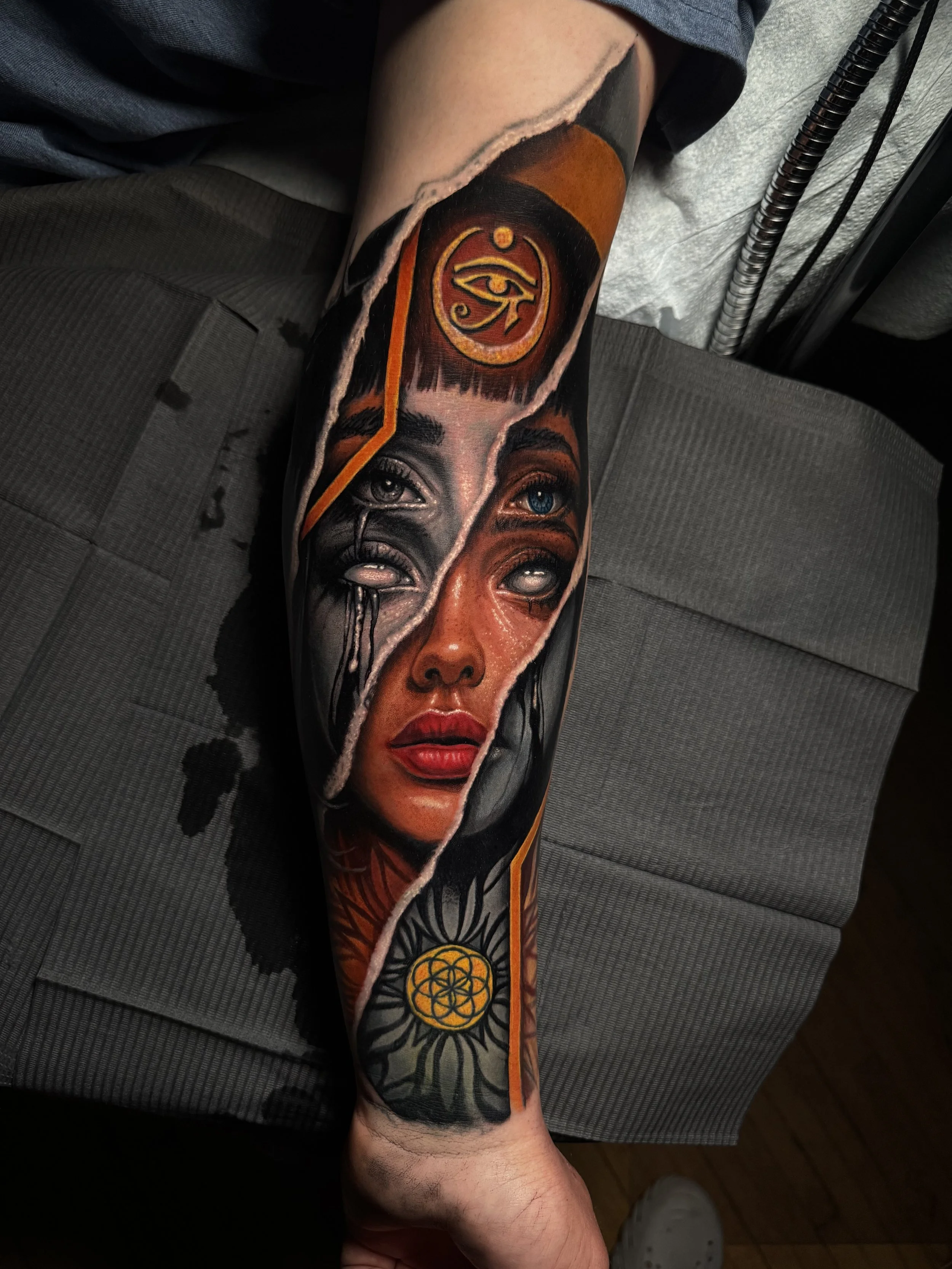 Daniel Armitage, Calgary Alberta, Surrealist Tattoo Artist | featuring a woman's face with an eye peeking through her forehead, with various spiritual and mystical symbols around her, including the Eye of Horus and a geometric design.