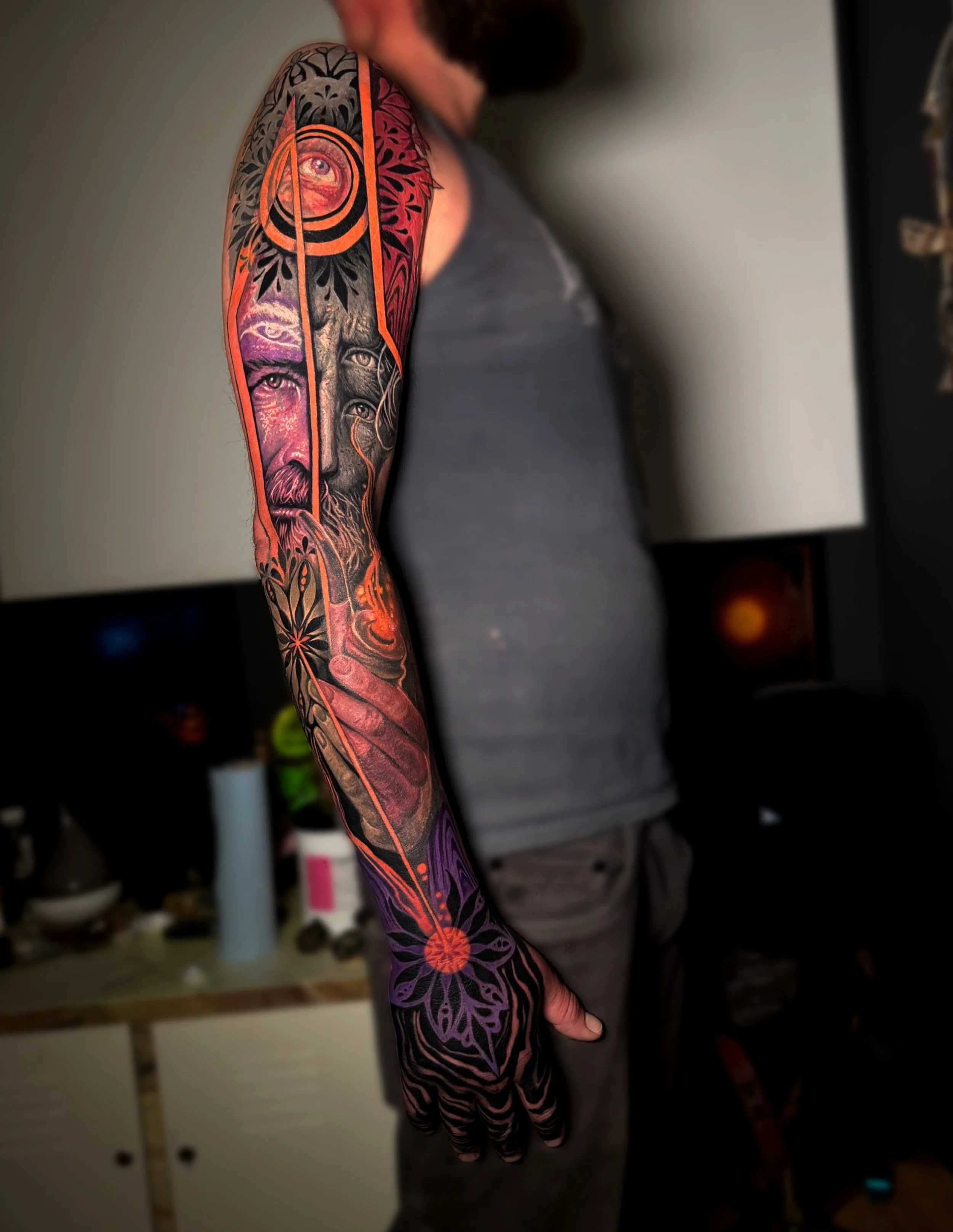 Daniel Armitage, Calgary Alberta, Surrealist Tattoo Artist, YYC Close-up of a person's arm with a colorful tattoo sleeve featuring human eyes, a face, floral designs, butterflies, and vibrant patterns.
