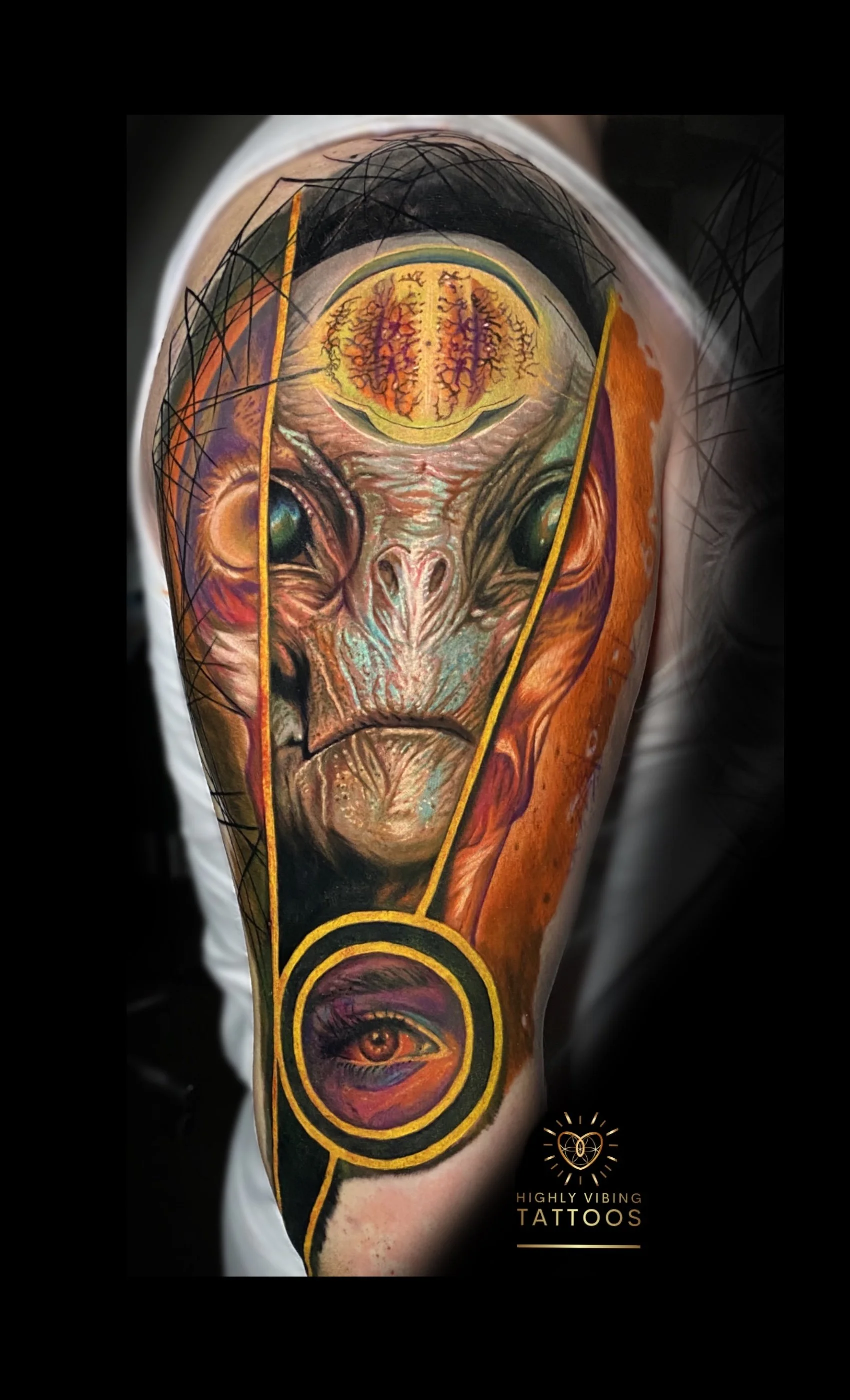 Close-up of a tattooed arm featuring a colorful, surreal composition including an alien-like face with large eyes and an intricate brain-like design above it, and a stylized eye at the bottom, with the text "Highly Vibing Tattoos" in the corner.
