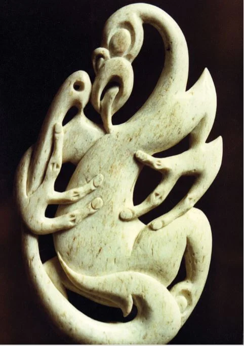 A carving from the jawbone of a sperm whale showing Tangaroa inspecting the artistry of a hei matau. The hook was let down to impress him so that he would reward the fisherman with a good catch of his children, the fish.