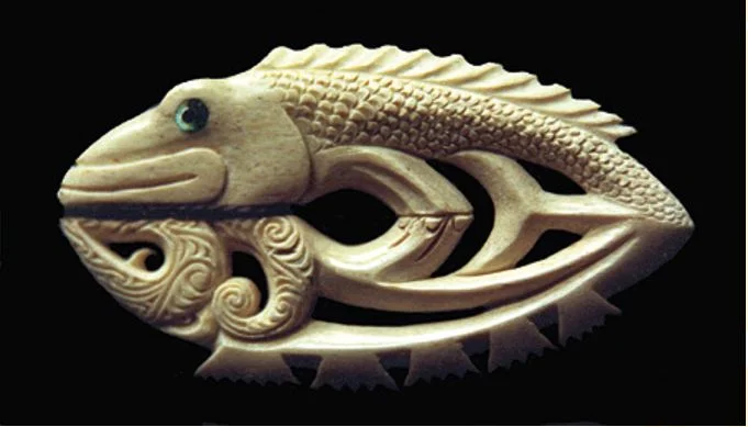 A fish looking at its reflection. The reflection is carved in the old Māori style, with dorsal fins represented as stylisations of face profiles.