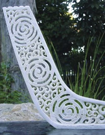 Carving of a stylised waka sternpost, showing a rainbow design at the top
