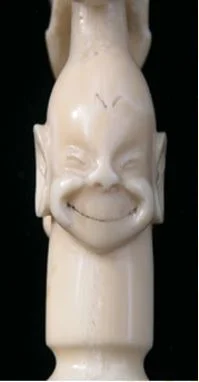 An Inuit dog whip handle carved in Alaska in the early 1900s by Happy Jack, showing detail of a Billiken