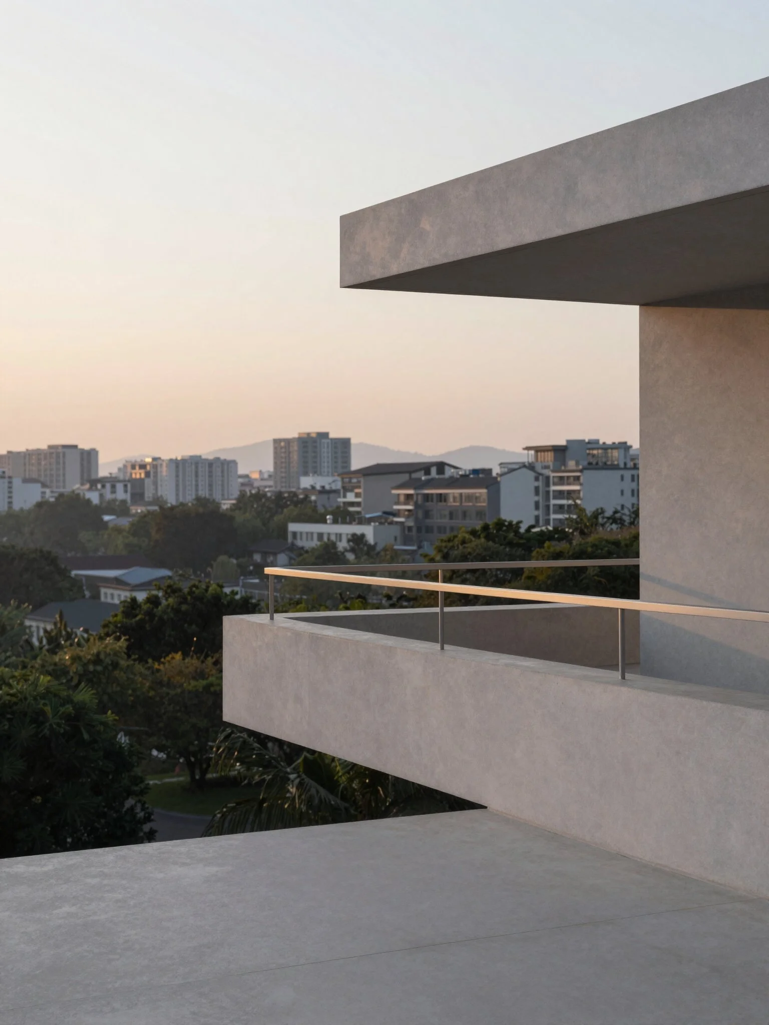 Modern balcony with concrete walls and metal railing, overlooking a cityscape at dusk with high-rise buildings and hills in the background.