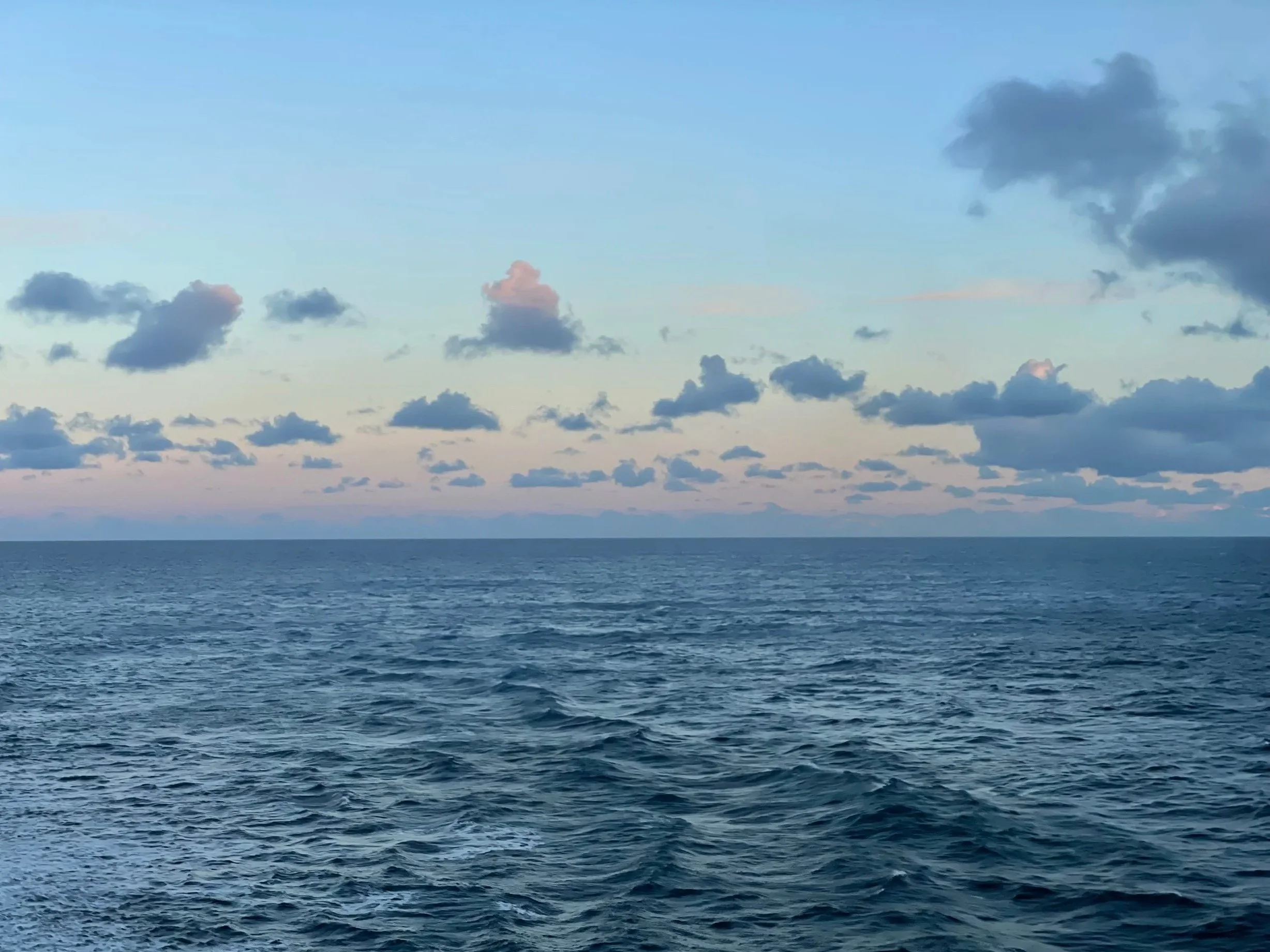 A vast ocean under a sky filled with scattered clouds during either sunrise or sunset.