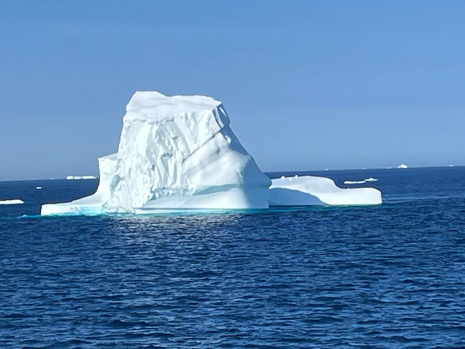 A large iceberg floating in the ocean with a clear blue sky above.