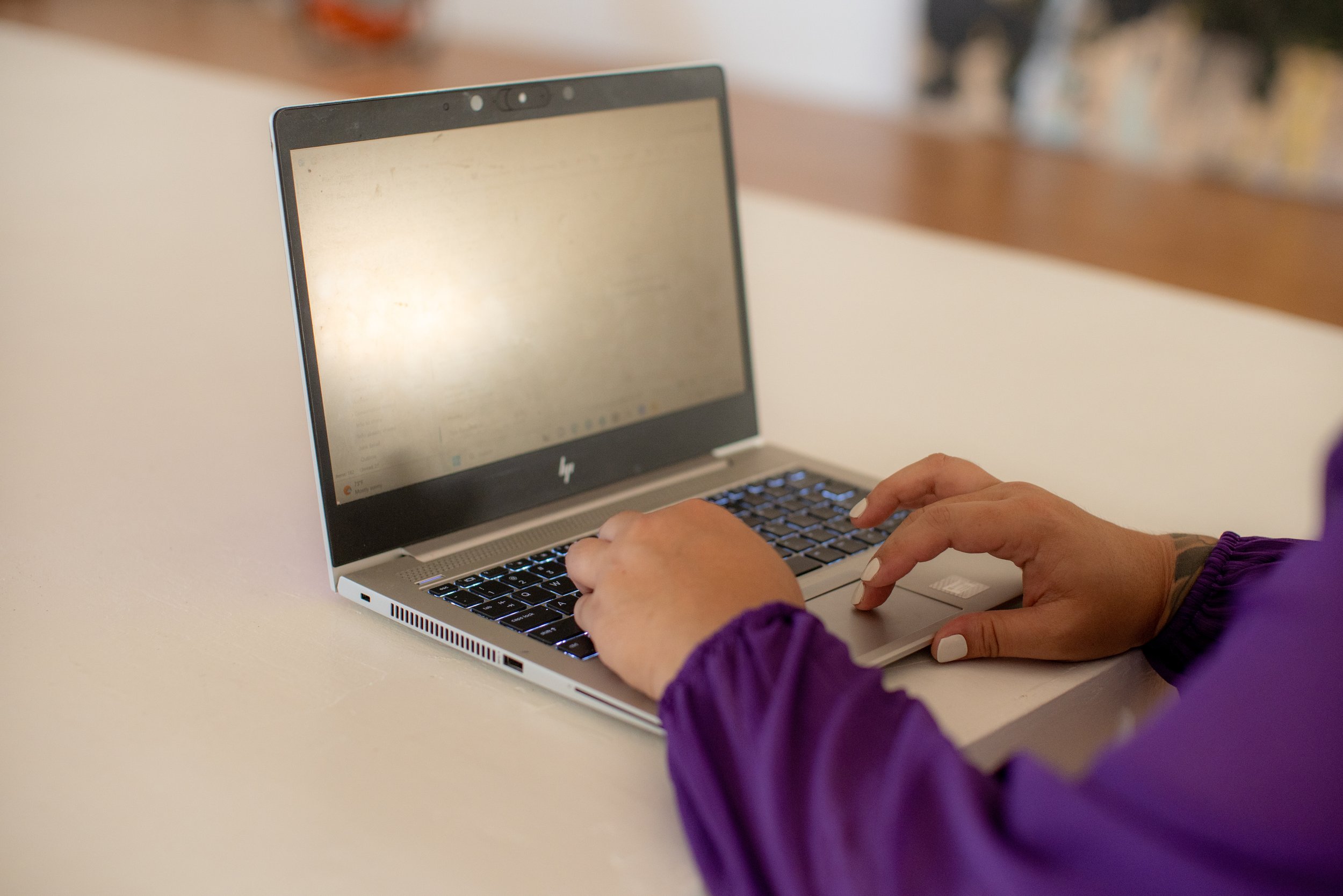 Person typing on a laptop with a purple jacket.