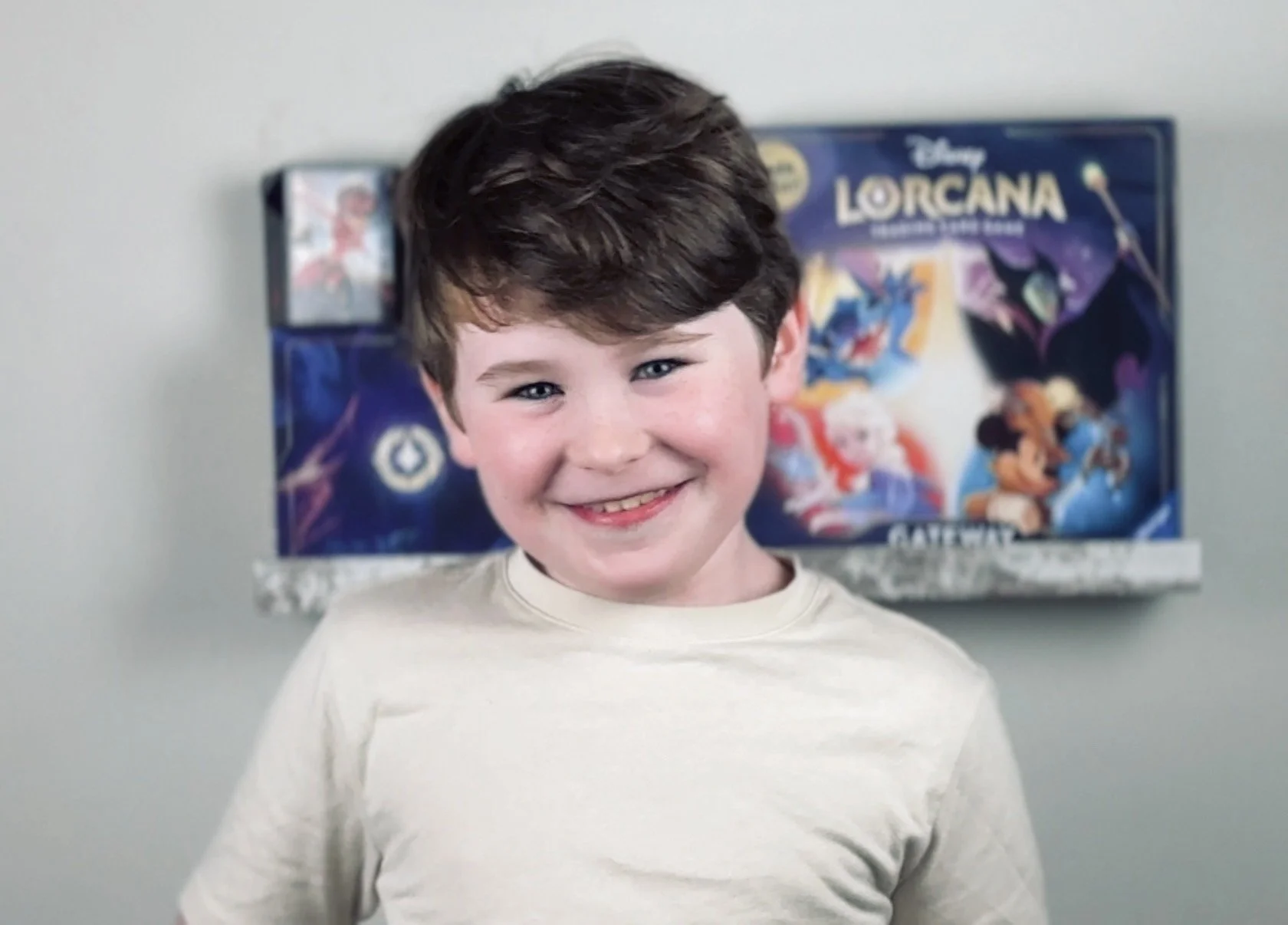 Young boy smiling in front of a Disney Lorcana game box.