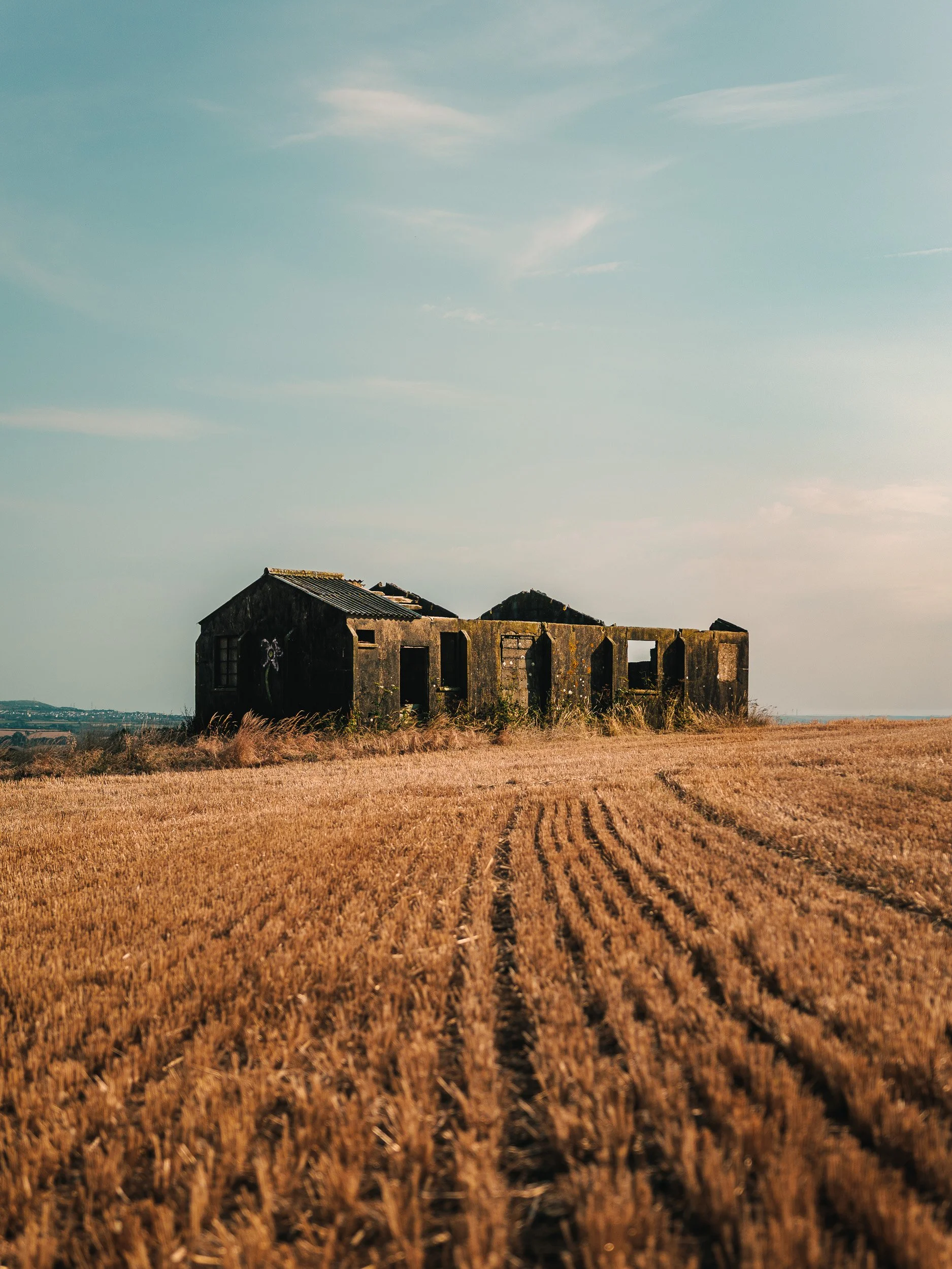 An abandoned, weathered barn in an open field under a cloudy sky.