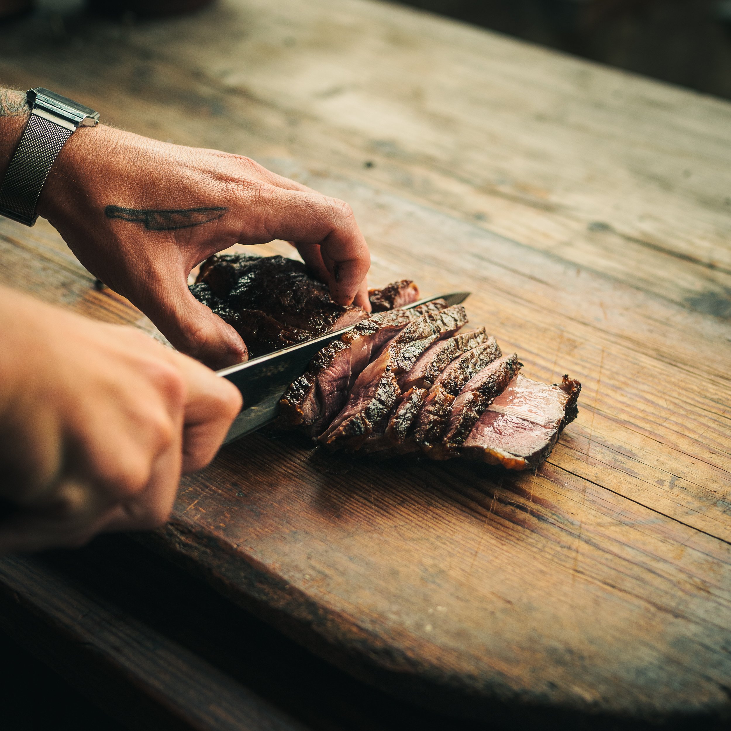 Close-up of a hand slicing a cooked meat roast on a wooden cutting board.