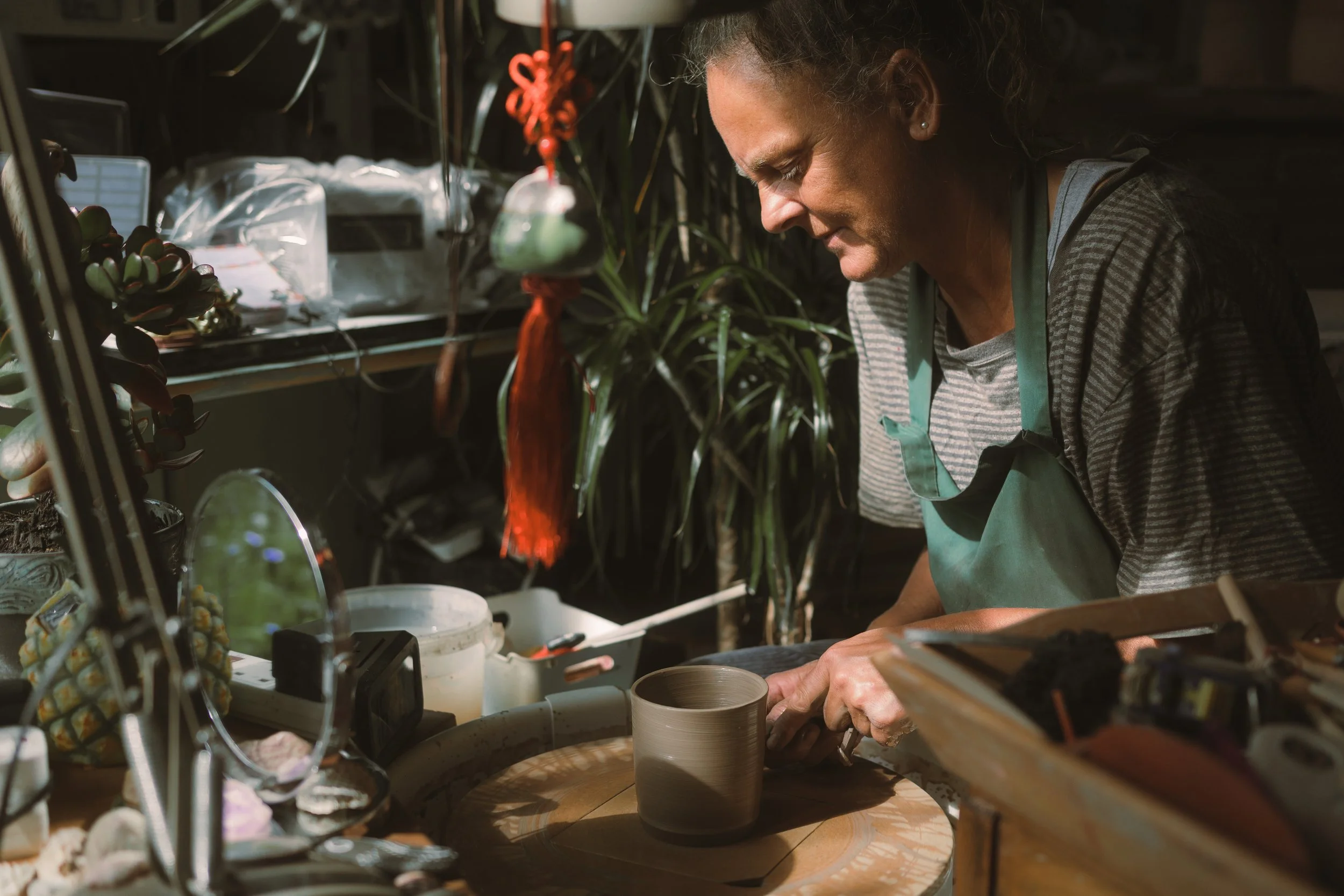 A woman working at a pottery wheel, shaping a clay piece in a ceramic studio.