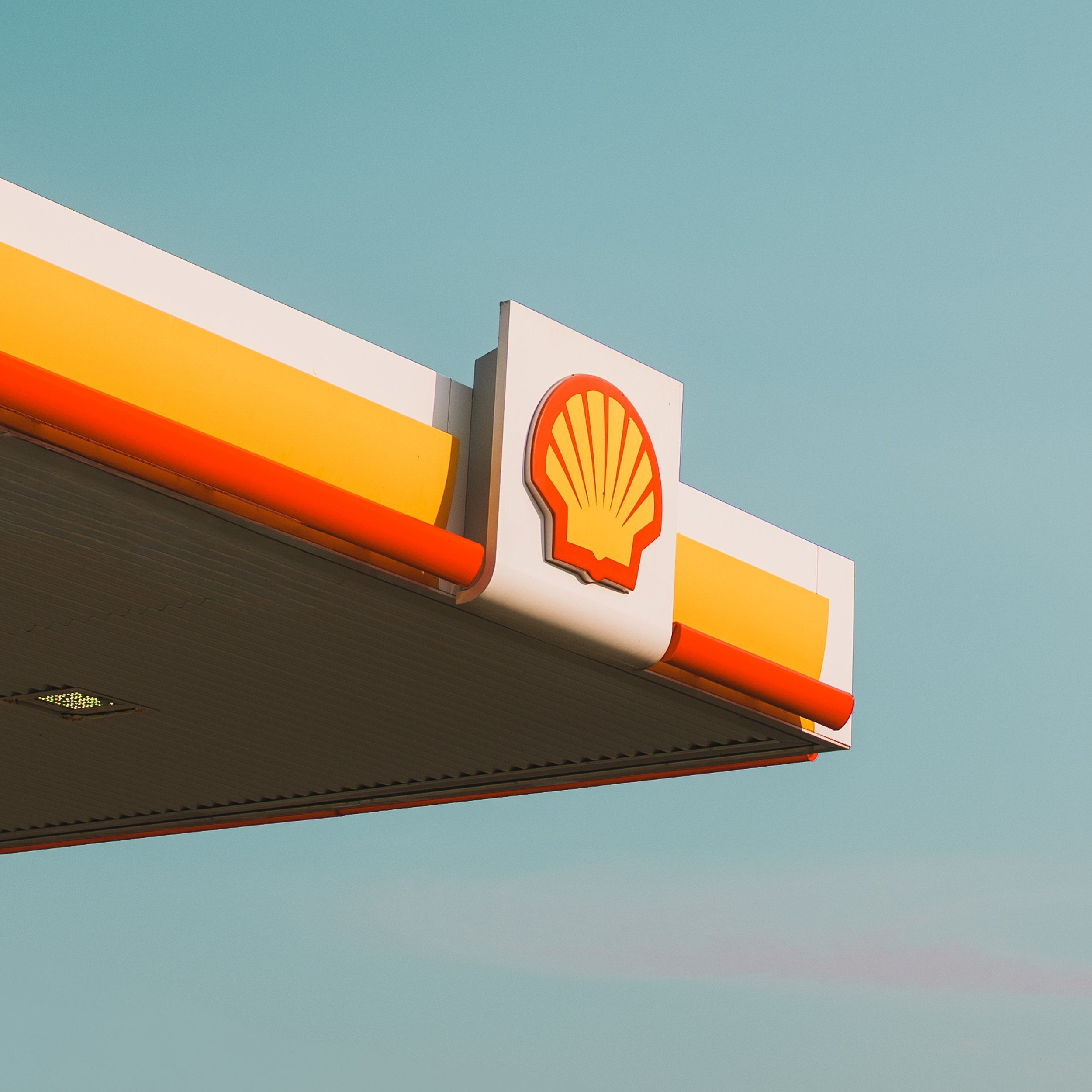 A Shell gas station sign with a yellow and orange shell logo on a light blue sky background.
