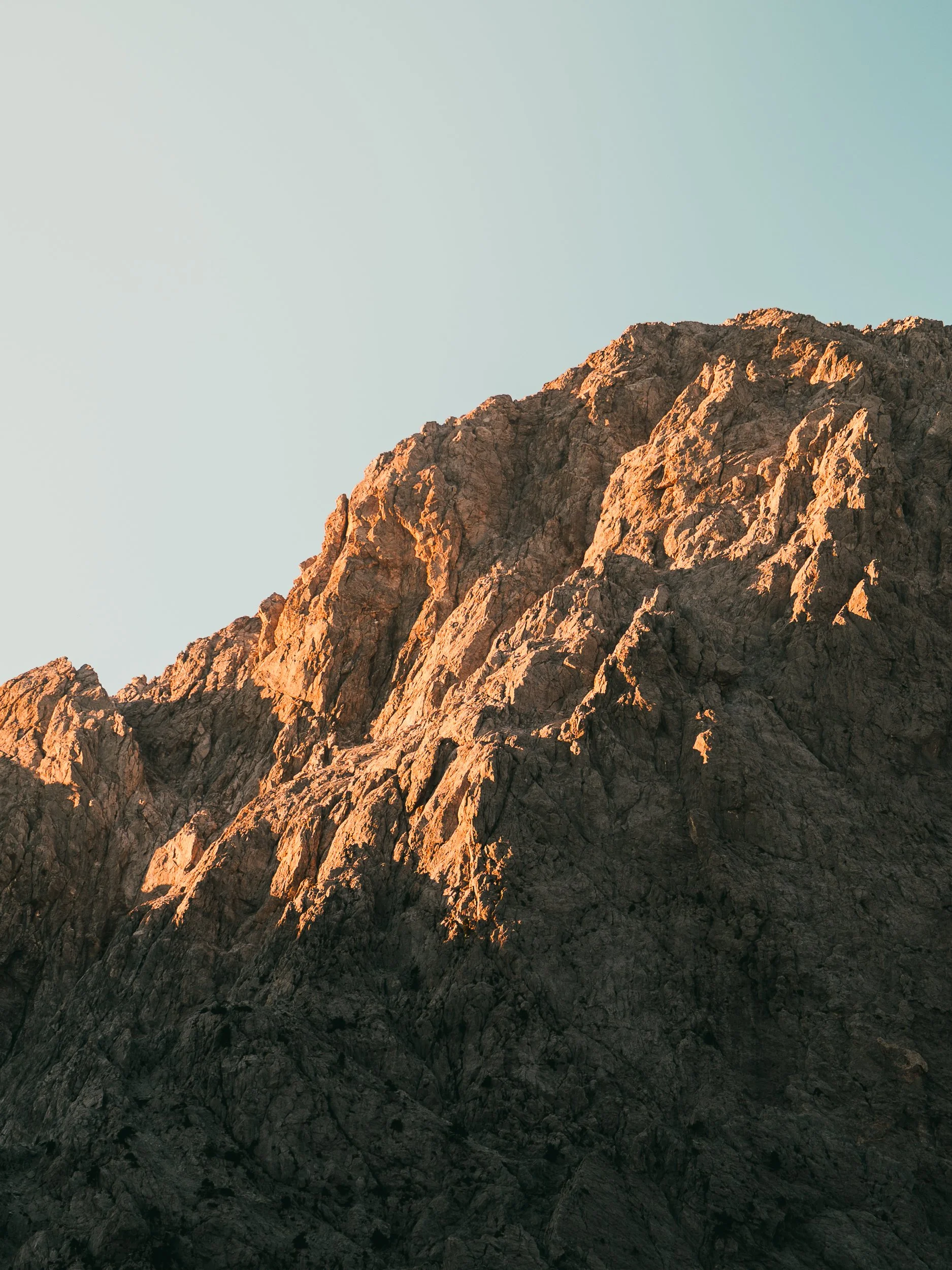 Close-up of rugged mountain peaks with sunlight highlighting the rocky surface, under a clear sky.