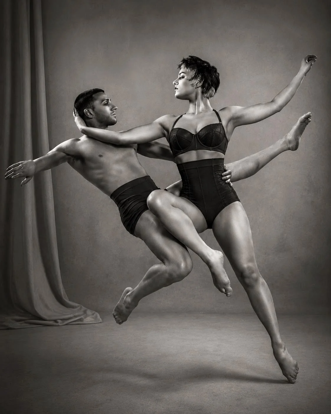 Black and white photo of a man and woman in dance poses with the woman lifting the man. They are dressed in dancewear, the woman in a leotard and the man in shorts.