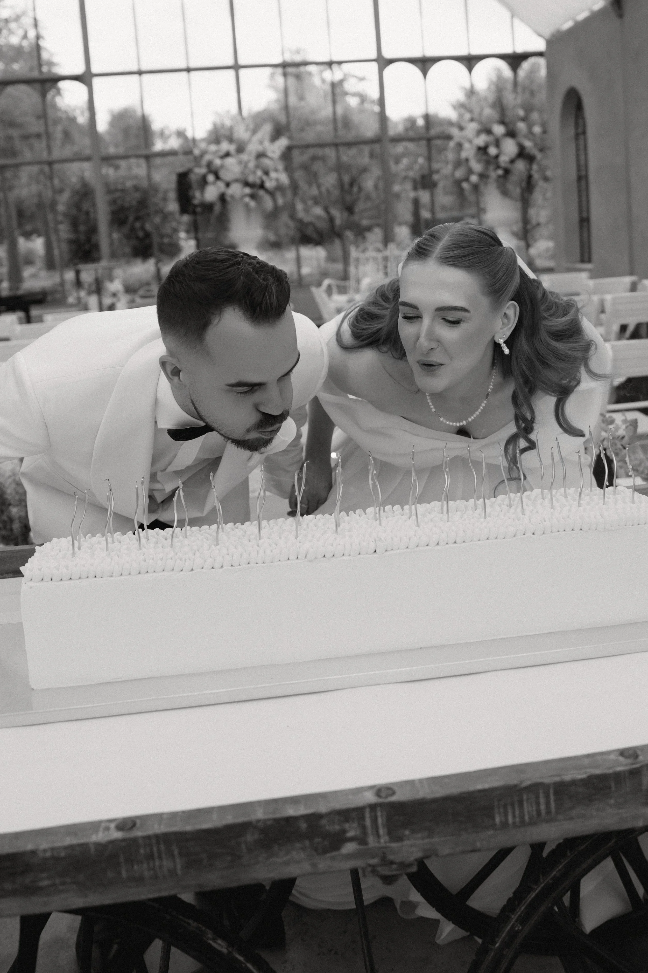 Es ist eine moderne, längliche Hochzeitstorte zu sehen. Die Hochzeitstorte ist zudem mit vielen Kerzen bestückt, ähnlich wie bei einer Geburtstagstorte. Das Brautpaar pustet die Kerzen gemeinsam aus.