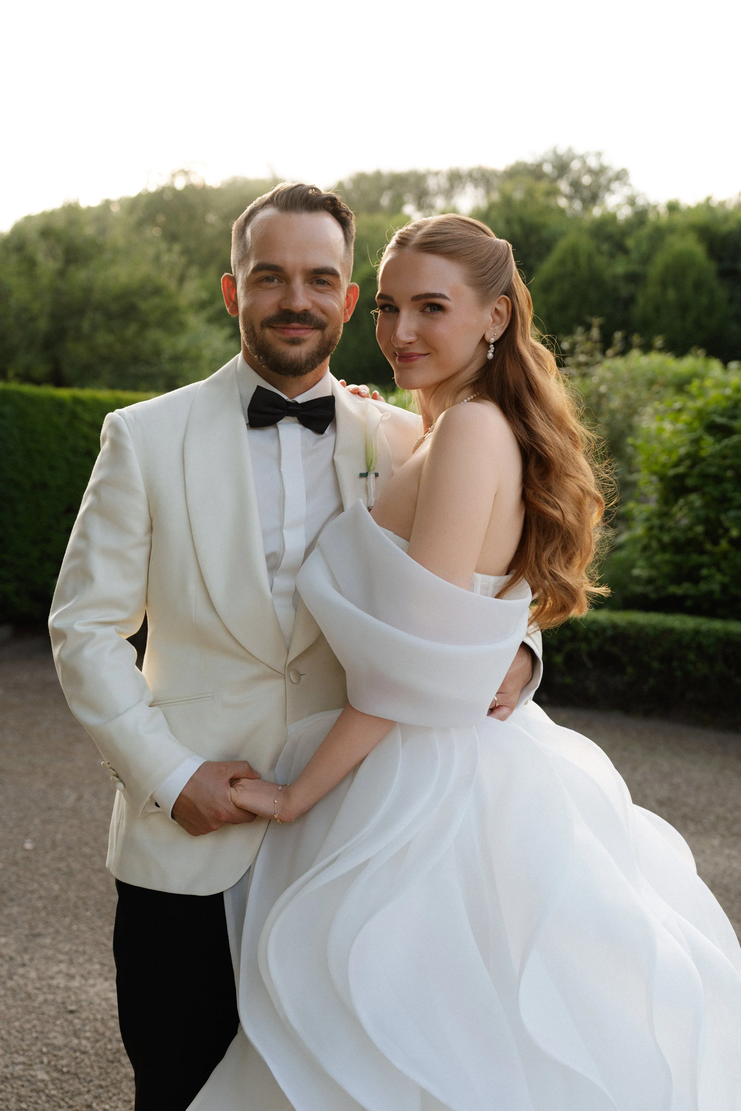 Braut und Bräutigam bei wunderschönem Licht im Portrait. Die Braut trägt das Designer Brautkleid "Bamnbina" von Milla Nova, der Bräutigam einen maßgeschneiderten Anzug mit schwarzer Hose und einem Sakko in ivory.