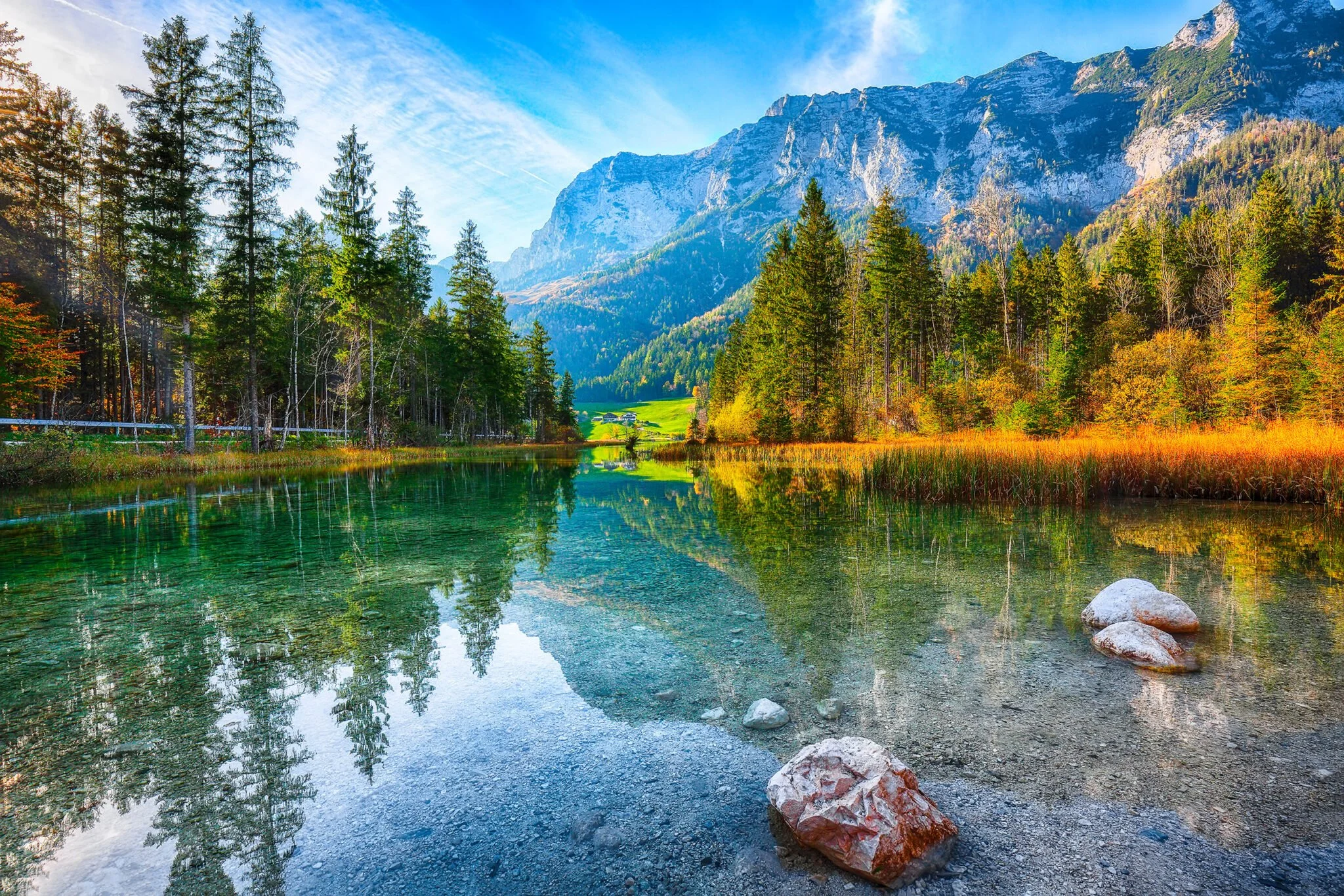 Bergsee im Herzen eines Waldes mit grünen Bäumen, darunter das klare Wasser des Sees, das die Berge im Hintergrund widerspiegelt, im Herbst mit bunten Blättern an den Bäumen.
