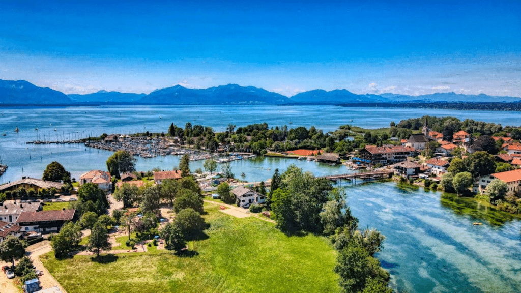 Luftaufnahme eines Dorfes am See mit Bergen im Hintergrund und einem Yachthafen.