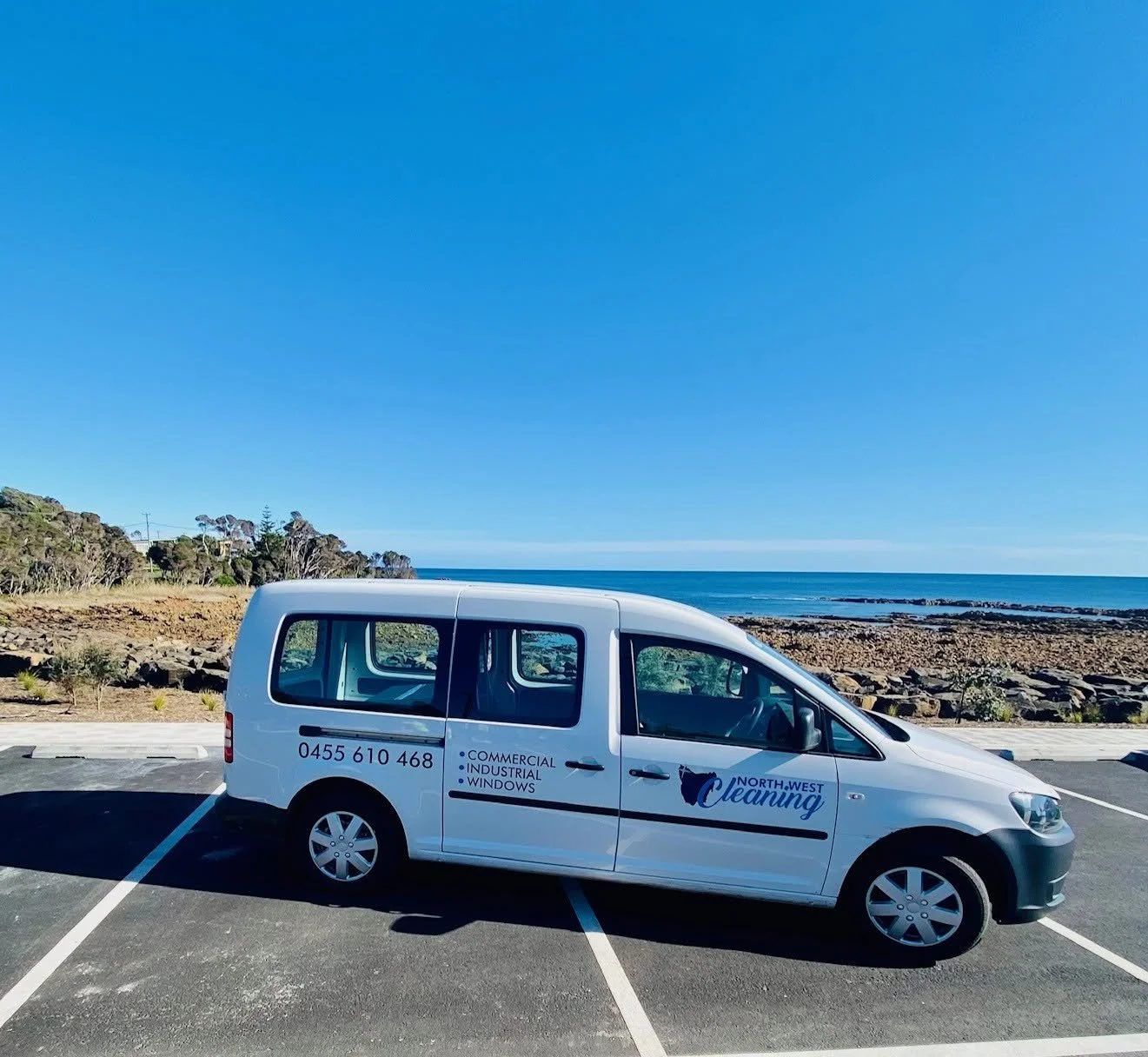 North West Cleaning service van parked beside a rocky ocean shoreline, advertising commercial and industrial window cleaning.
