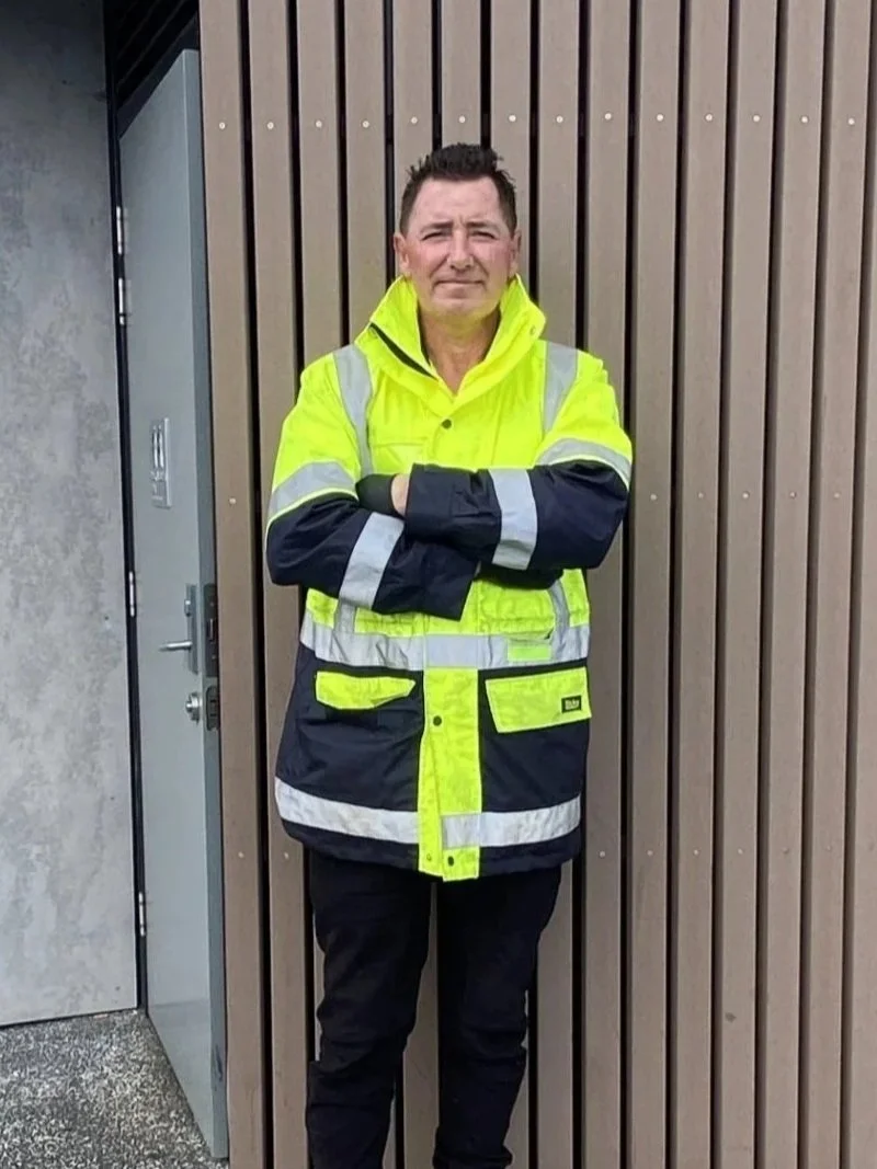 Worker wearing a high-visibility neon yellow safety jacket standing with crossed arms outside a building