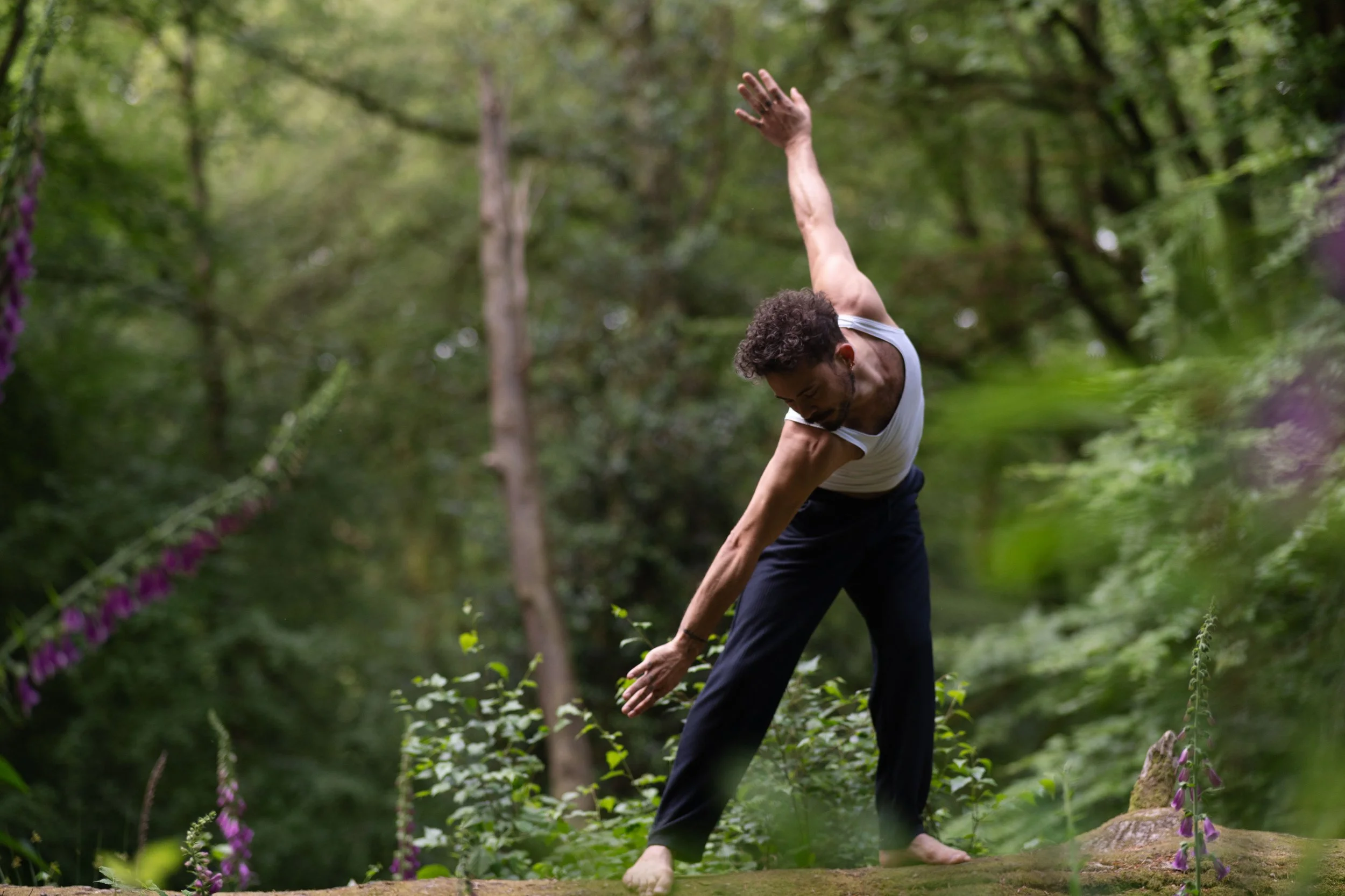 A man practicing yoga outdoors on a wooden platform surrounded by trees and greenery.