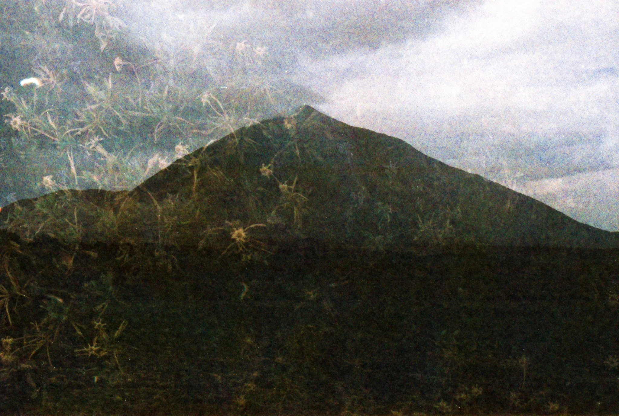 Nighttime view of a mountain with a stormy sky, some clouds, and faint lightning in the distance.