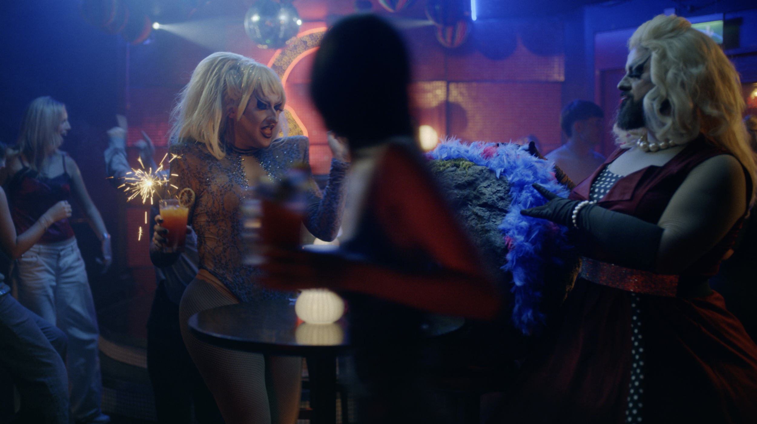 People dancing and celebrating in a lively nightclub with colorful lighting and disco balls.