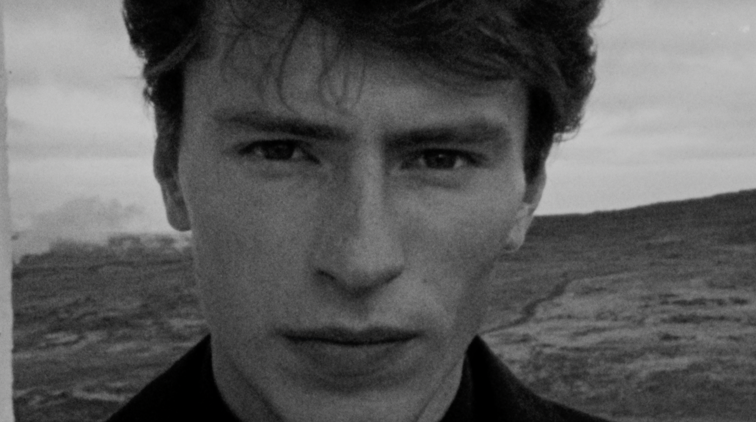 Black and white close-up photo of a young man with dark hair, partially submerged in water, with only his face visible.