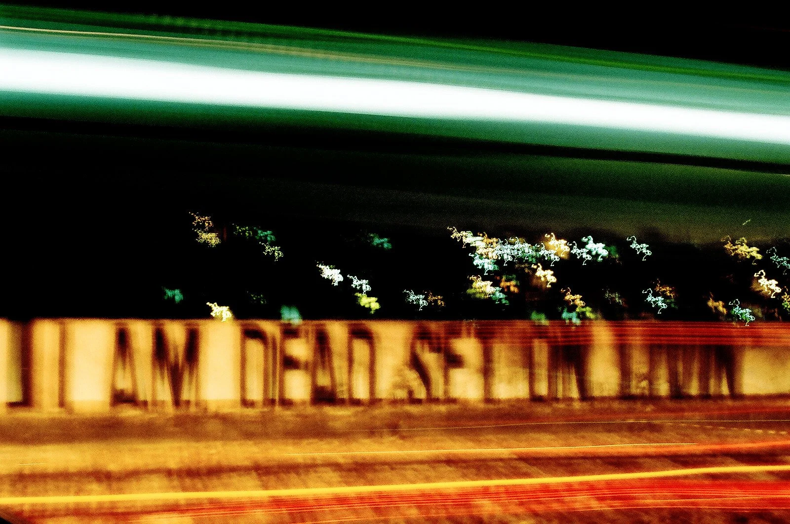 Blurred night scene of a bridge with the word 'AMERICA' visible, with city lights in the background and streaks of light from moving vehicles.