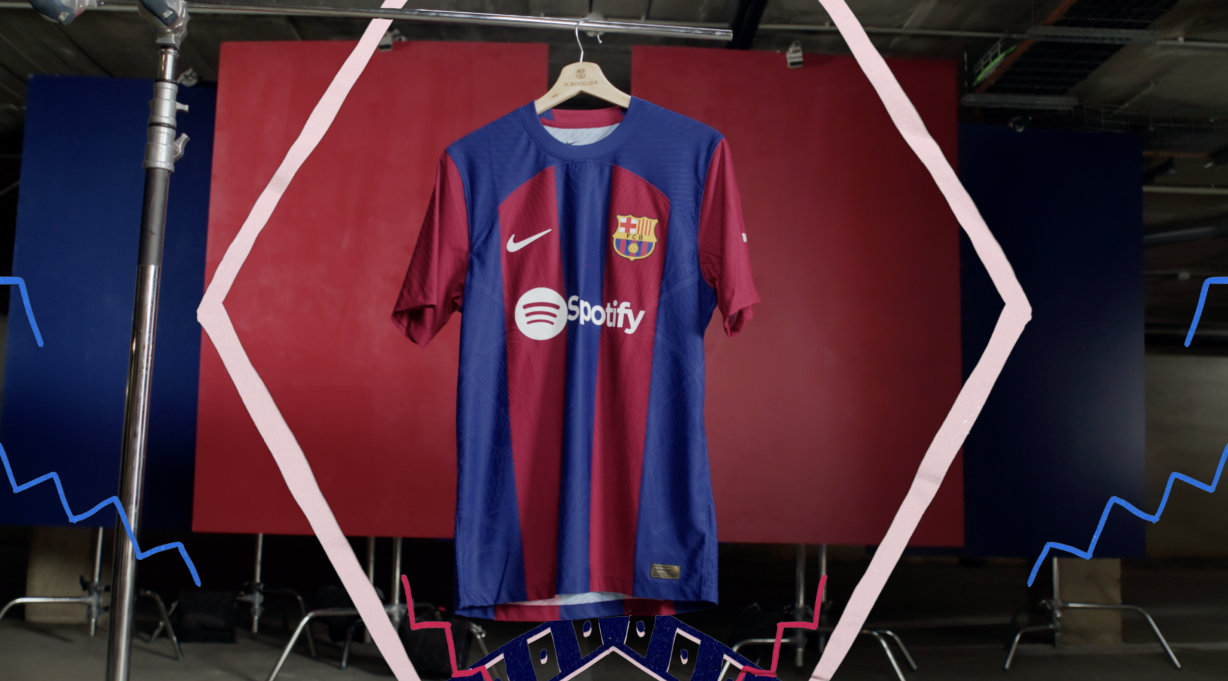 A FC Barcelona soccer jersey hanging on a hanger against a red and blue background with a pink zigzag border and graphic elements.