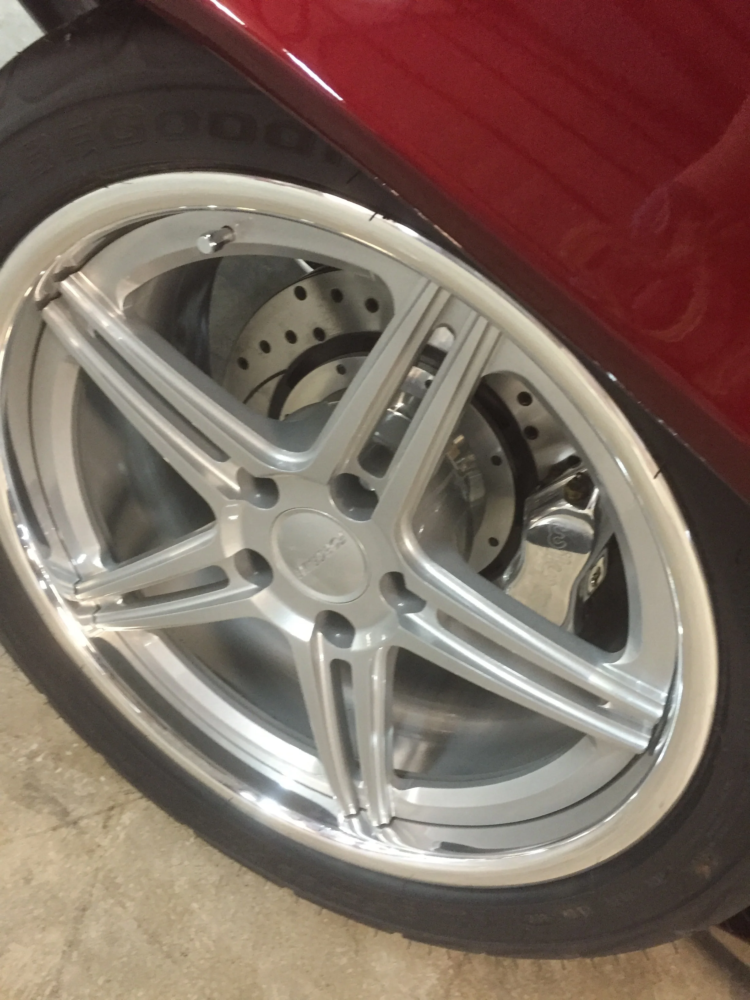 Close-up of a silver car wheel with a black tire and red car body above.