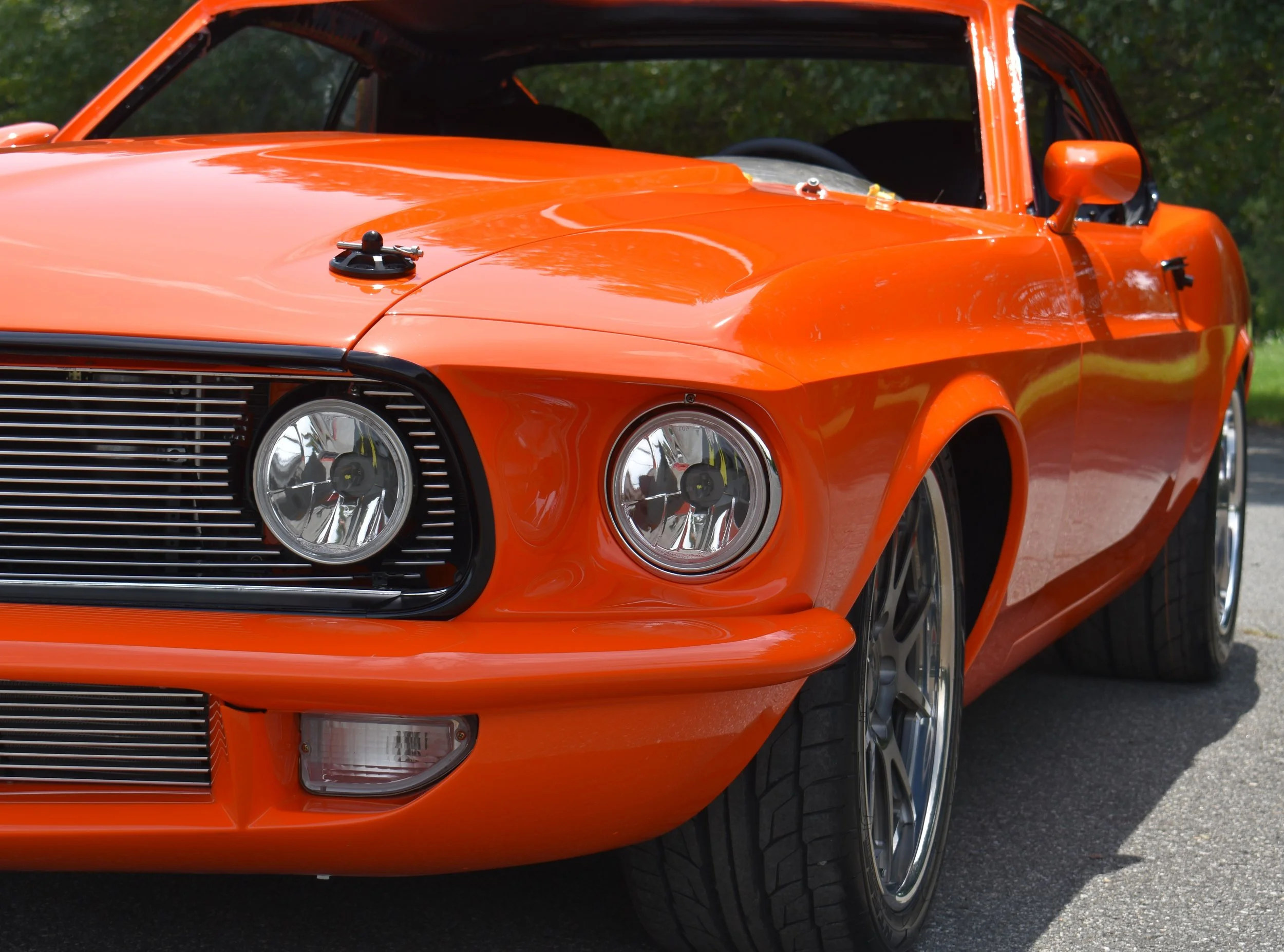 A bright orange sports car parked outdoors with the front and side visible, featuring sleek design, round headlights, and a shiny finish.