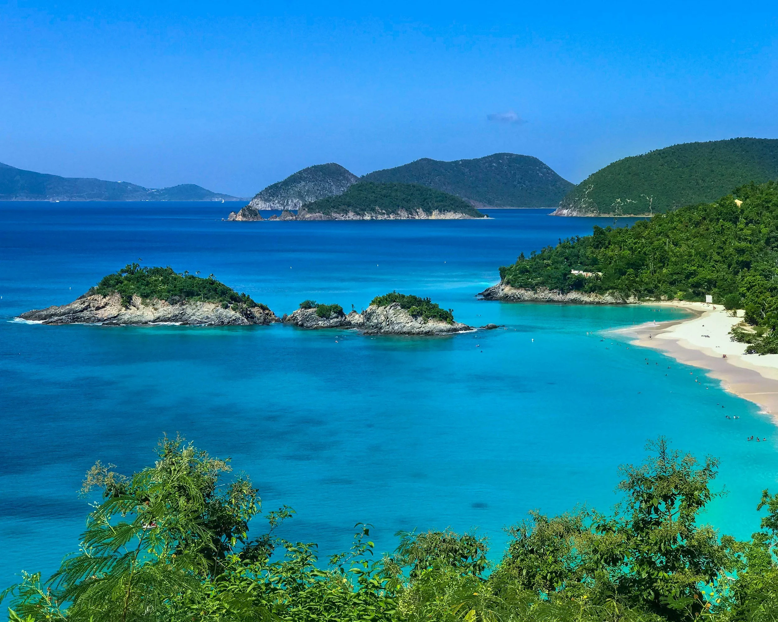 urquoise bay with green hills, rocky islets and a sandy beach.